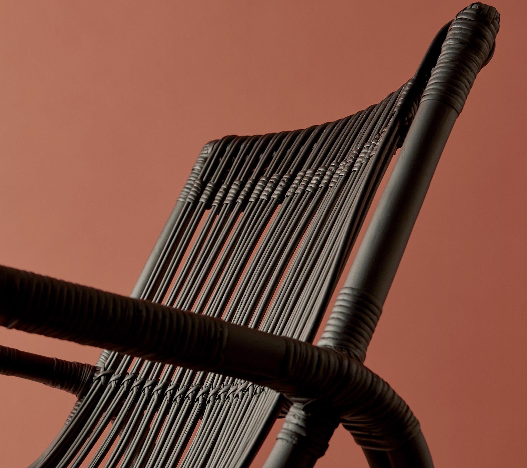 A close-up view of a woven chair backrest against a warm-colored background, highlighting its intricate design and texture.