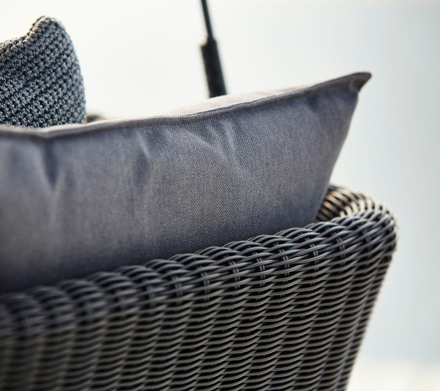 Close-up of a woven basket-style chair featuring a textured dark gray cushion, emphasizing comfort and modern design.