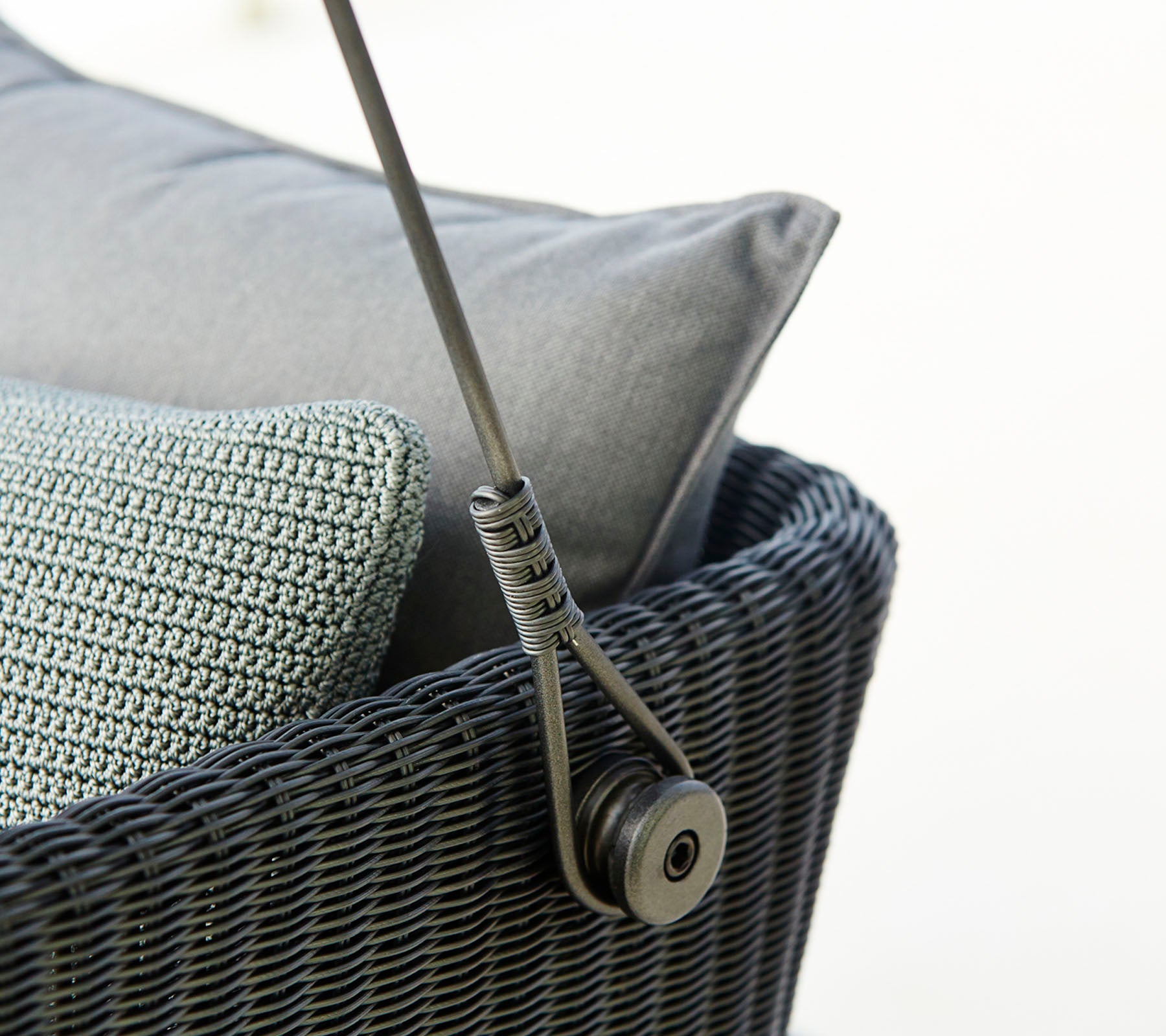 Close-up of a stylish woven seating piece featuring grey pillows and a sleek support mechanism. Ideal for modern decor.