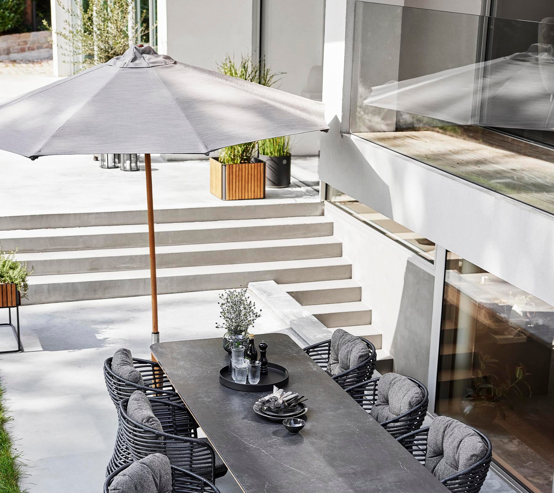 A stylish outdoor dining setup featuring a long table, basket chairs, and a classic parasol for shade.