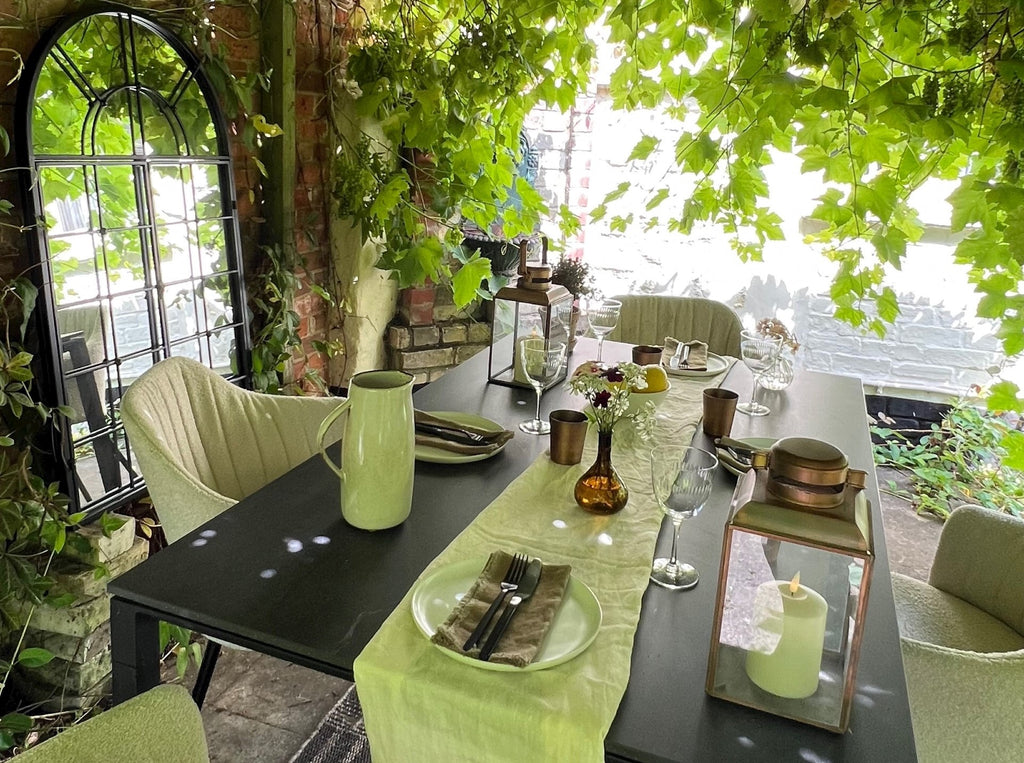 dining setting under a green grapevine pergola in the garden. Sand bouclé outdoor dining chairs and black ceramic table from Cane-line