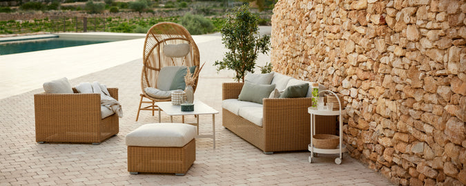 Modern outdoor lounge setting featuring brown rattan sofa and chairs with beige cushions.