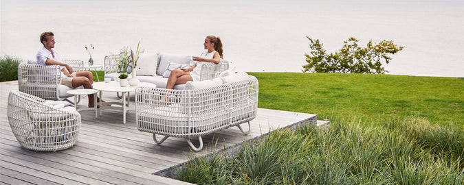 Modern white outdoor sofa and armchair set on a wooden deck overlooking greenery.