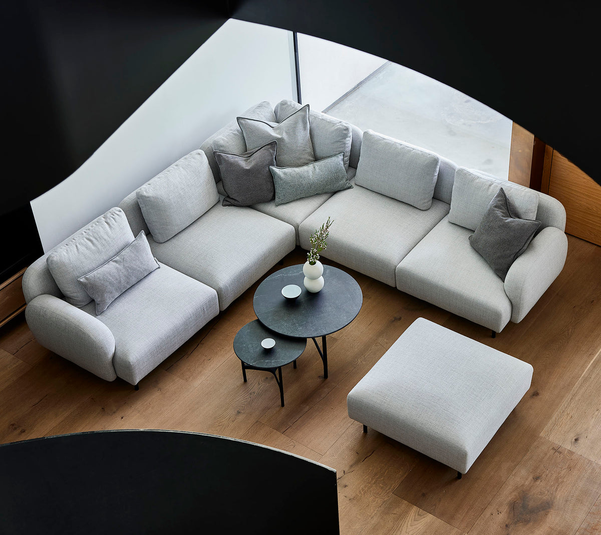 Stylish gray sectional sofa with decorative pillows, accompanied by a sleek round coffee table and an ottoman on a wooden floor.