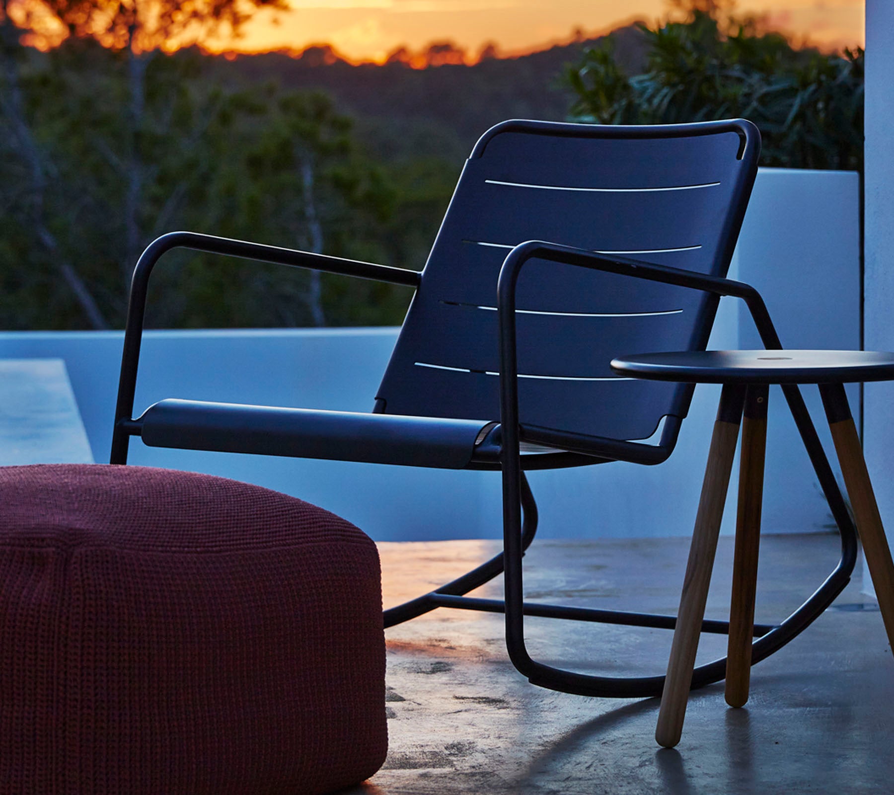 Stylish rocking chair with a sleek black frame and gray seat cushion, accompanied by a small wooden side table and a round pouf.