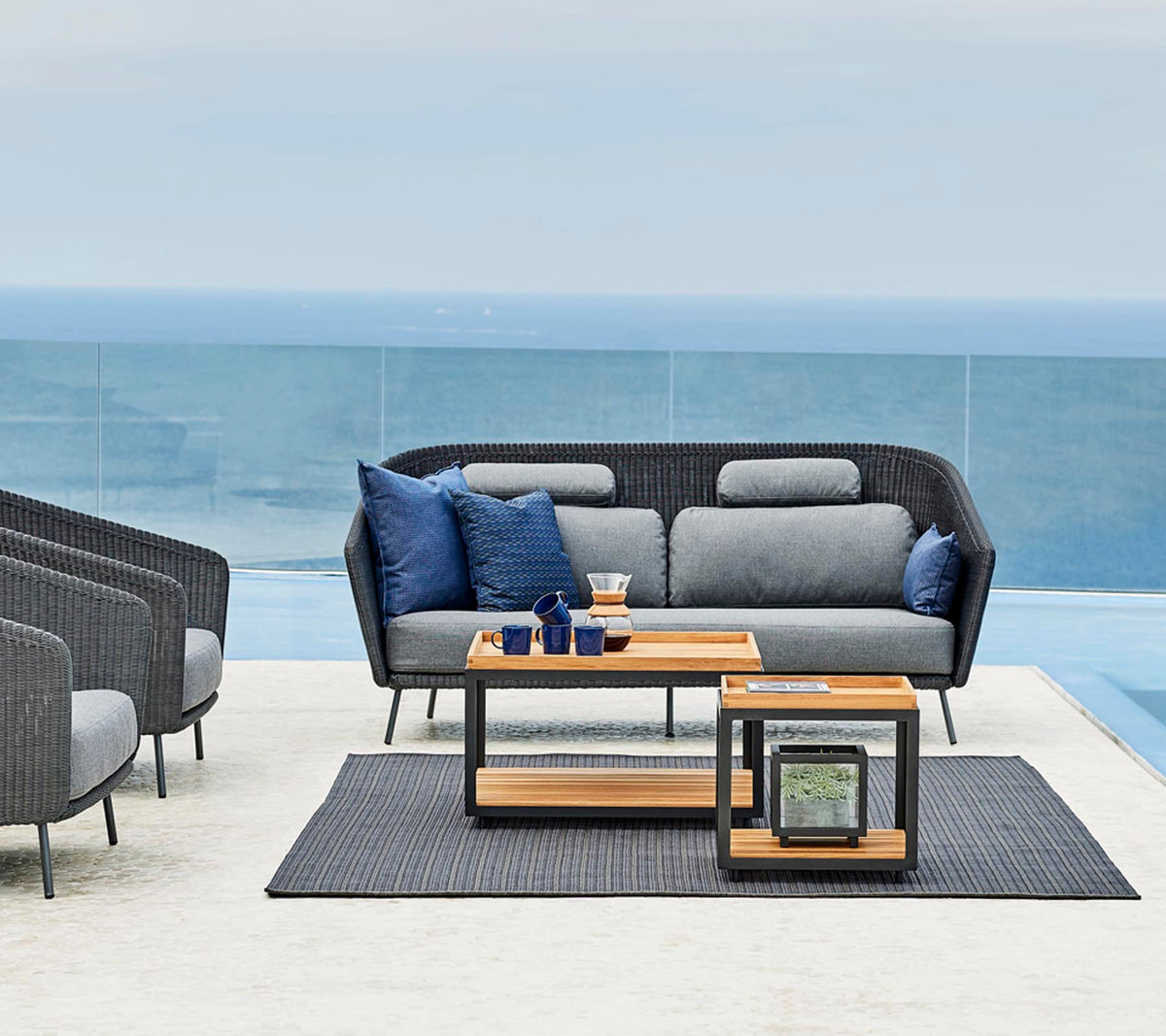 Stylish outdoor seating arrangement featuring a gray sofa with blue cushions, a wooden side table, and a matching rug.