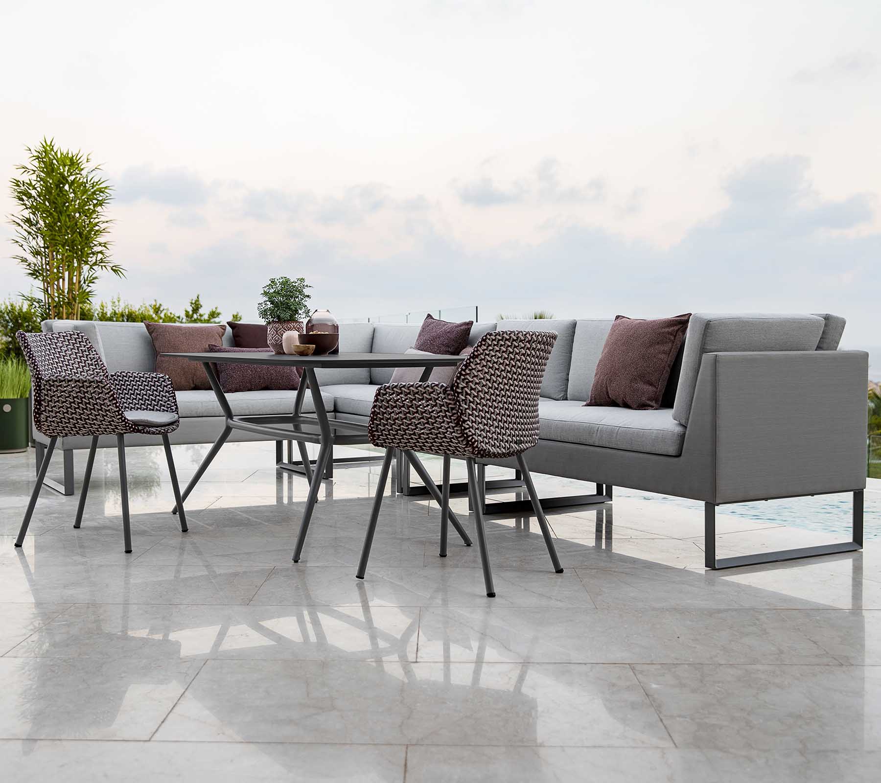 Modern outdoor seating arrangement featuring a sectional sofa with cushions, a glass-top table, and stylish chairs.