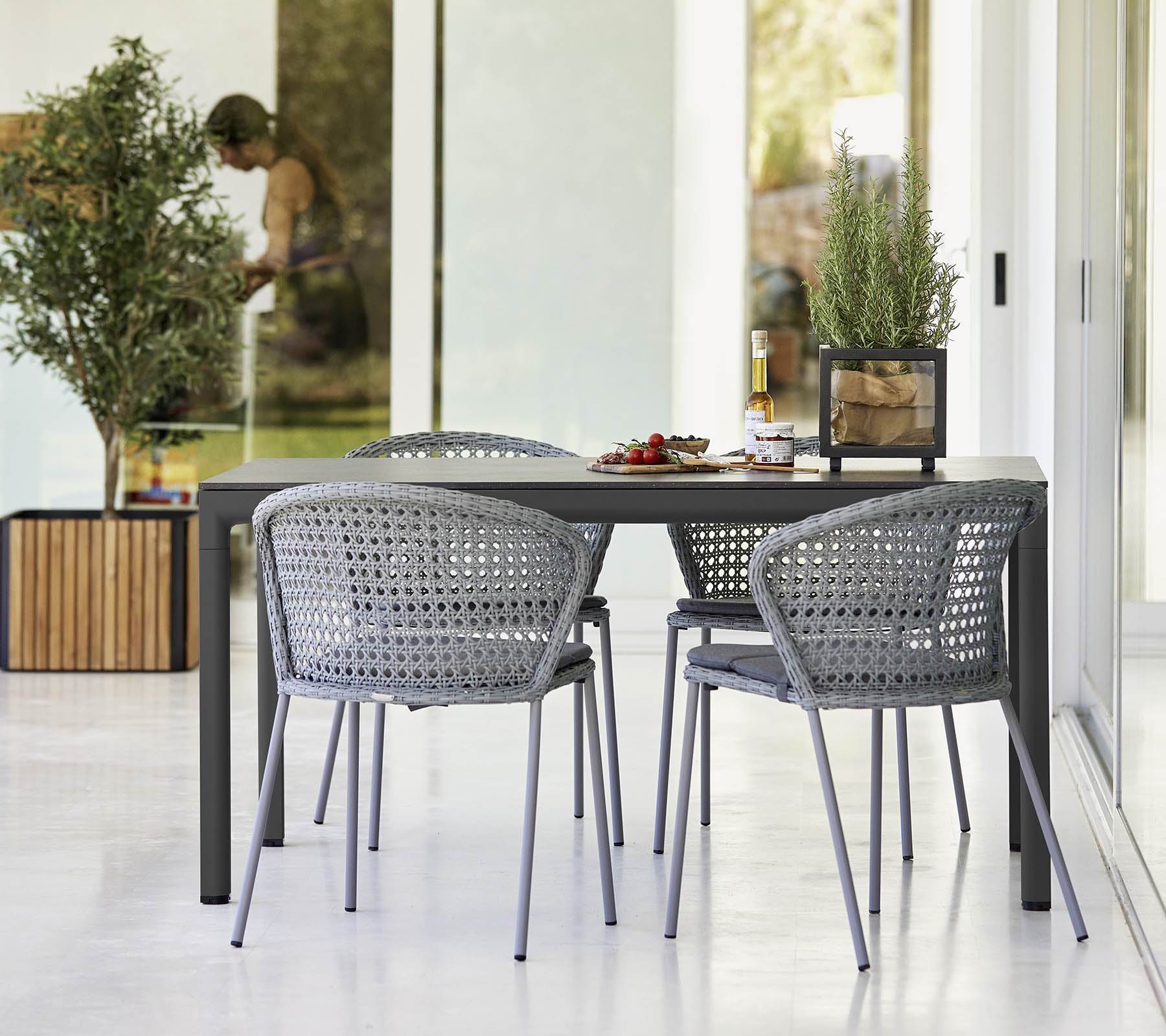 Modern table set with four gray woven chairs, adorned with small plants and a decorative centerpiece. Bright and inviting ambiance.
