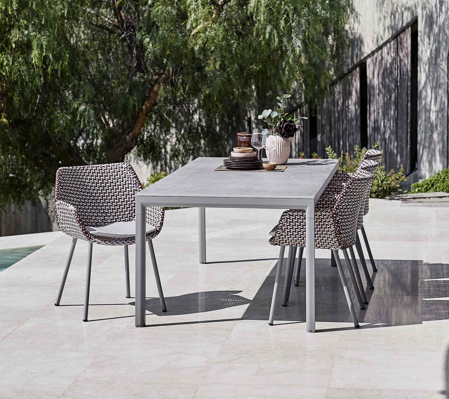 A modern dining table surrounded by stylish woven chairs, complemented by decorative vases and greenery in the background.