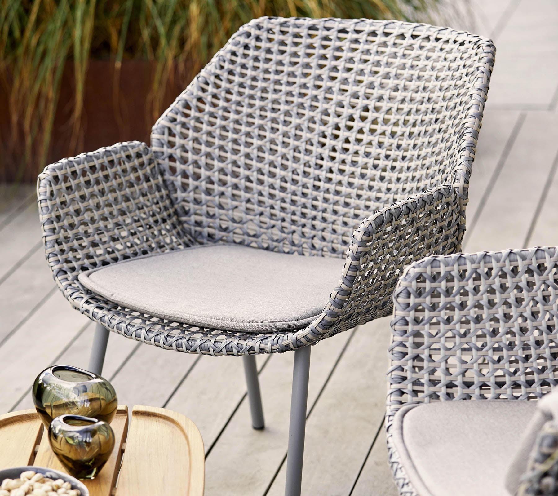Stylish woven chair in light gray with a comfortable cushion, complemented by decorative vases and a wooden serving tray.