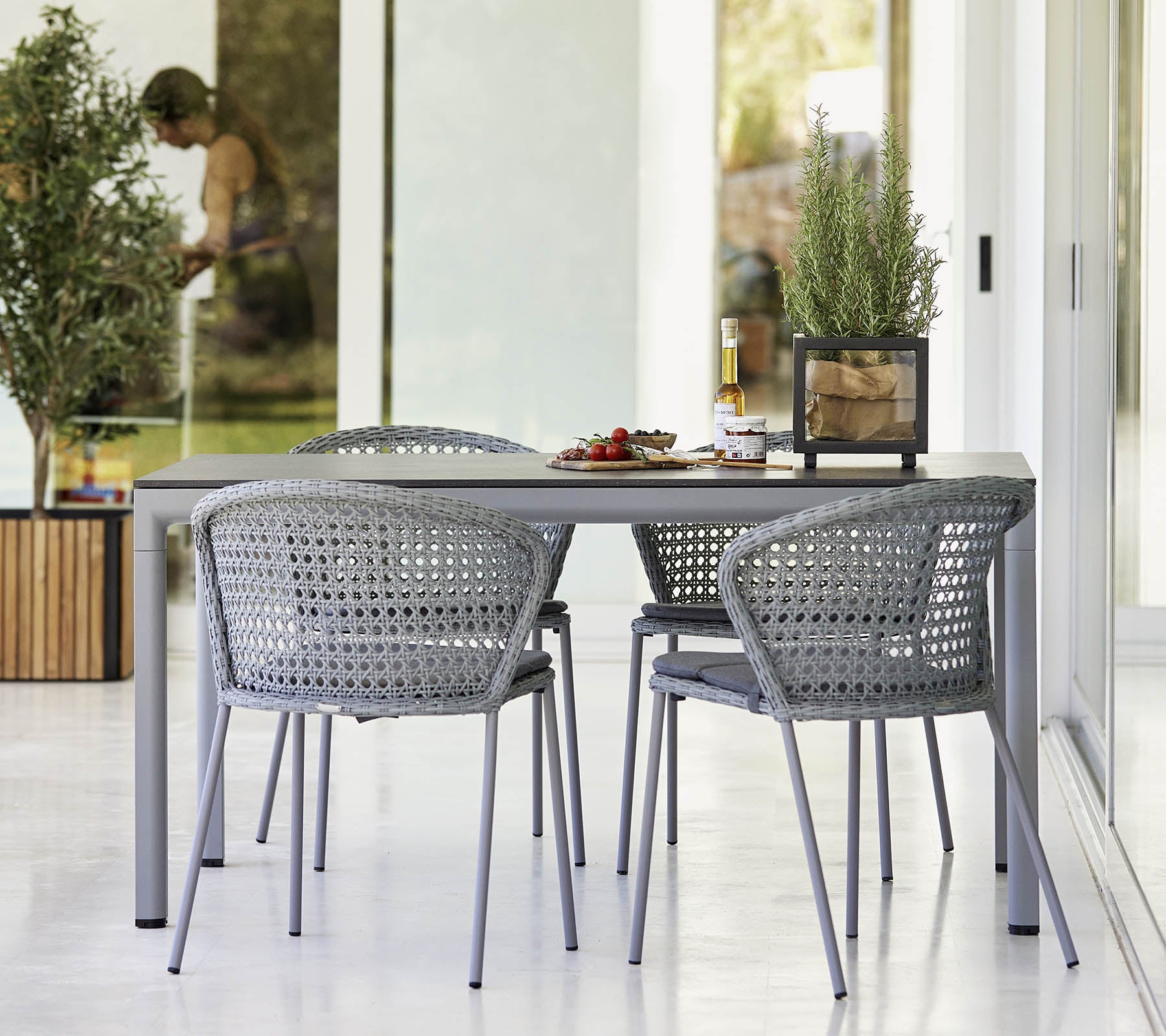 Modern dining set featuring a sleek table and woven chairs, complemented by greenery and a light, airy atmosphere.