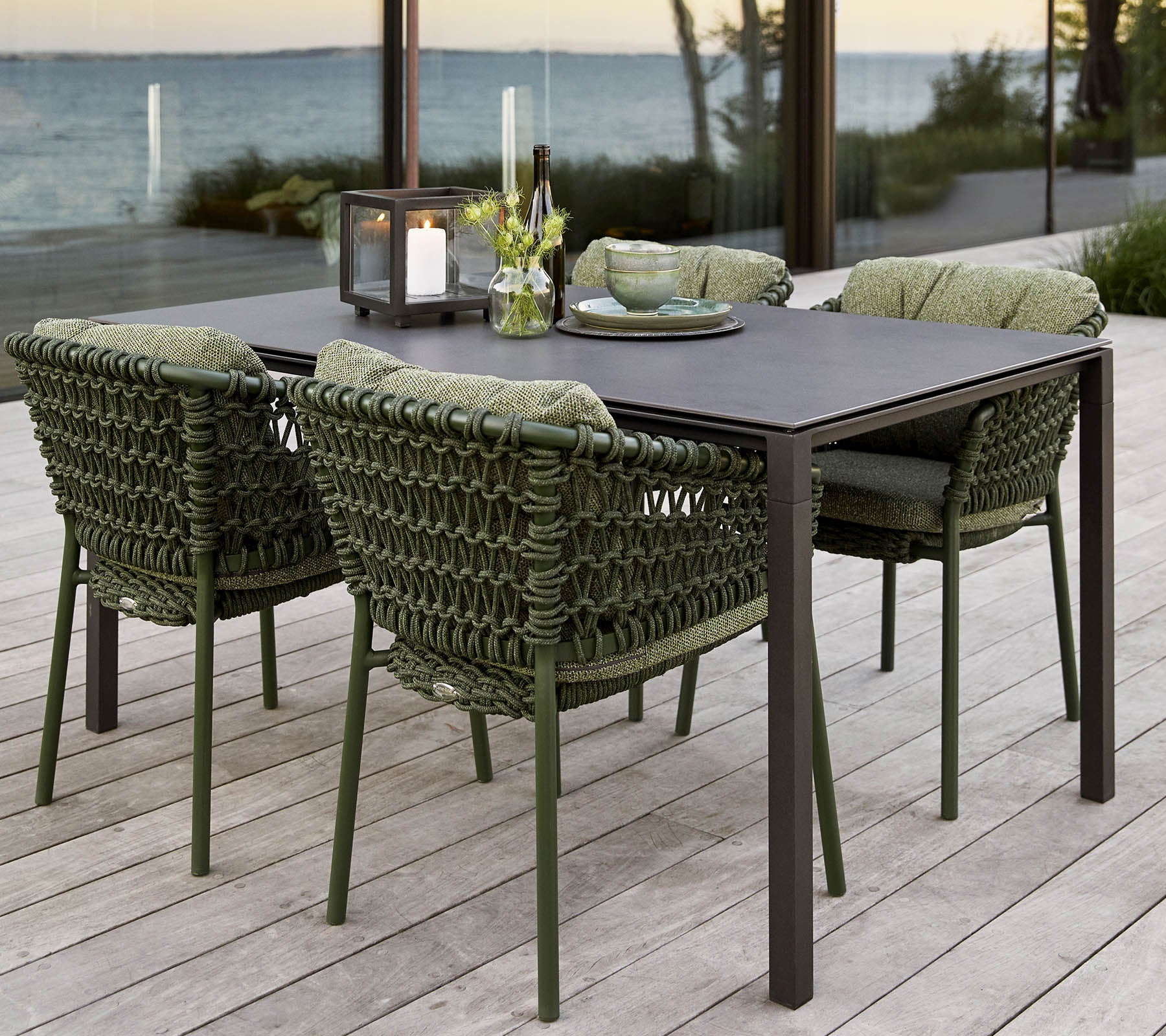 Stylish outdoor dining set featuring a rectangular table and four cushioned, woven chairs, complemented by a centerpiece of flowers.