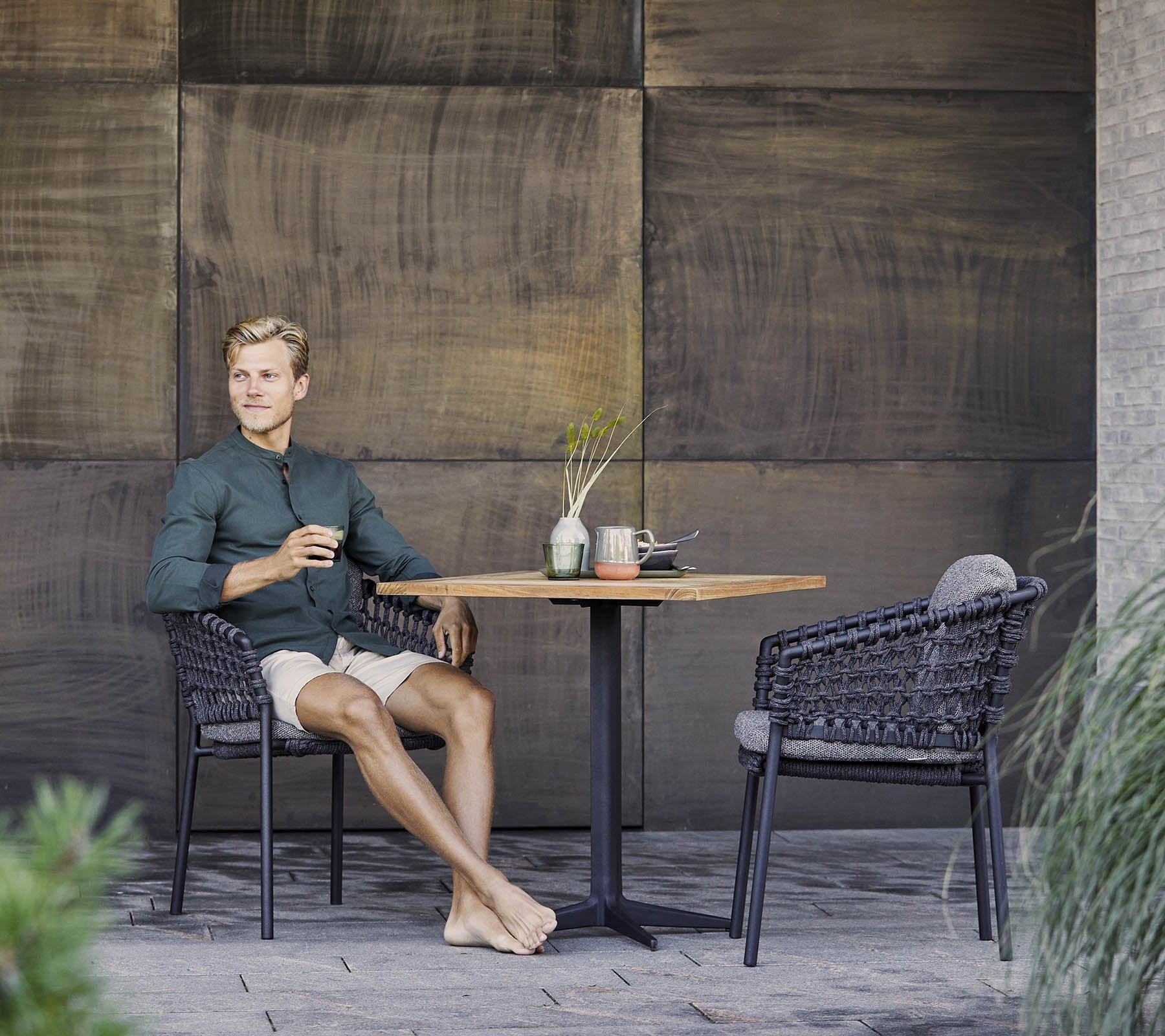 A person sits relaxed at a table, enjoying a drink, surrounded by stylish wicker chairs and decorative elements.
