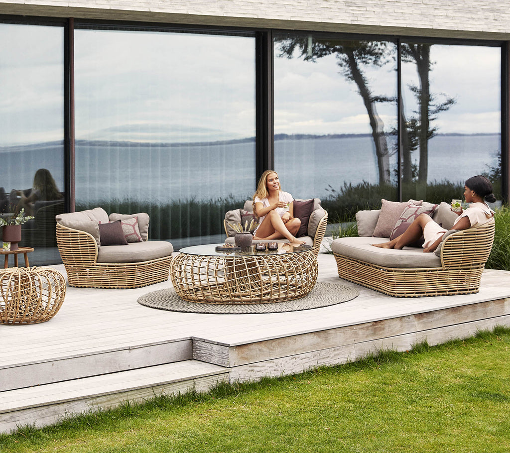 A stylish rattan seating area with cushions, featuring a coffee table and serene views in the background, ideal for relaxation.