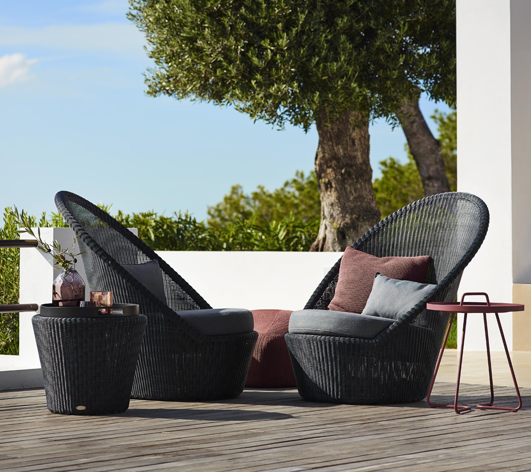 Two stylish black woven chairs with plush cushions, accompanied by a small matching table, set against a natural backdrop.