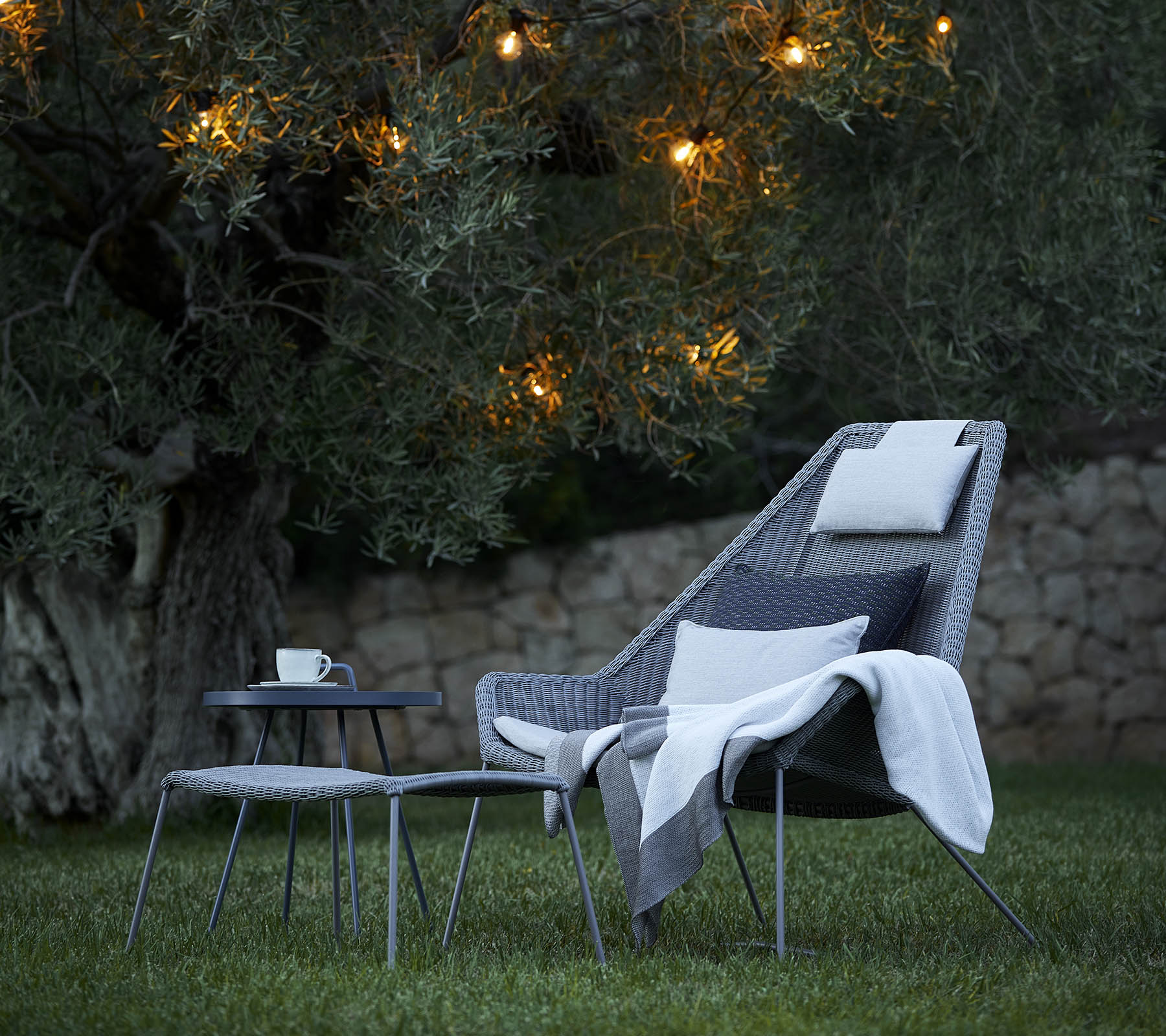 Stylish seating arrangement with a cozy chair, soft throw, and side table, illuminated by soft lights in the backdrop.
