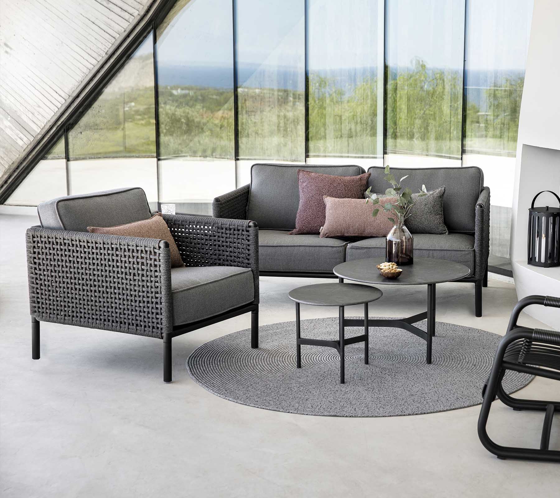 Stylish seating arrangement featuring a grey sofa and armchair with cushions, accompanied by a round table on a textured rug.