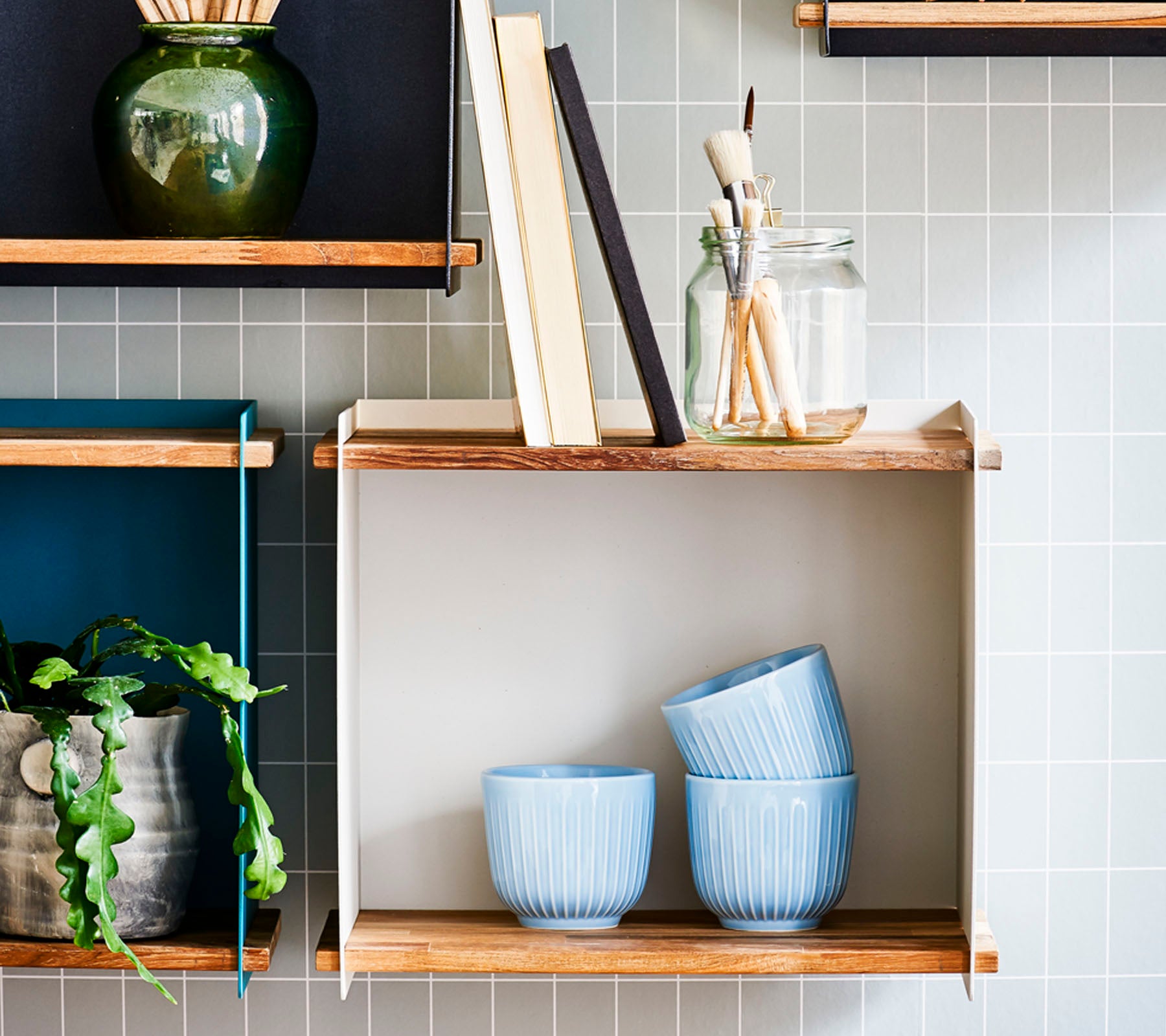 Shelves with decorative items, including blue bowls, books, a jar with brushes, and a potted plant against a tiled background.