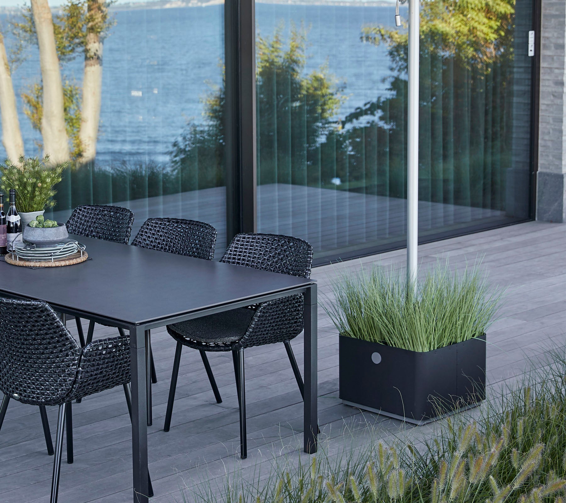 A stylish table with chairs set beside a water view, featuring a decorative planter with lush grass.