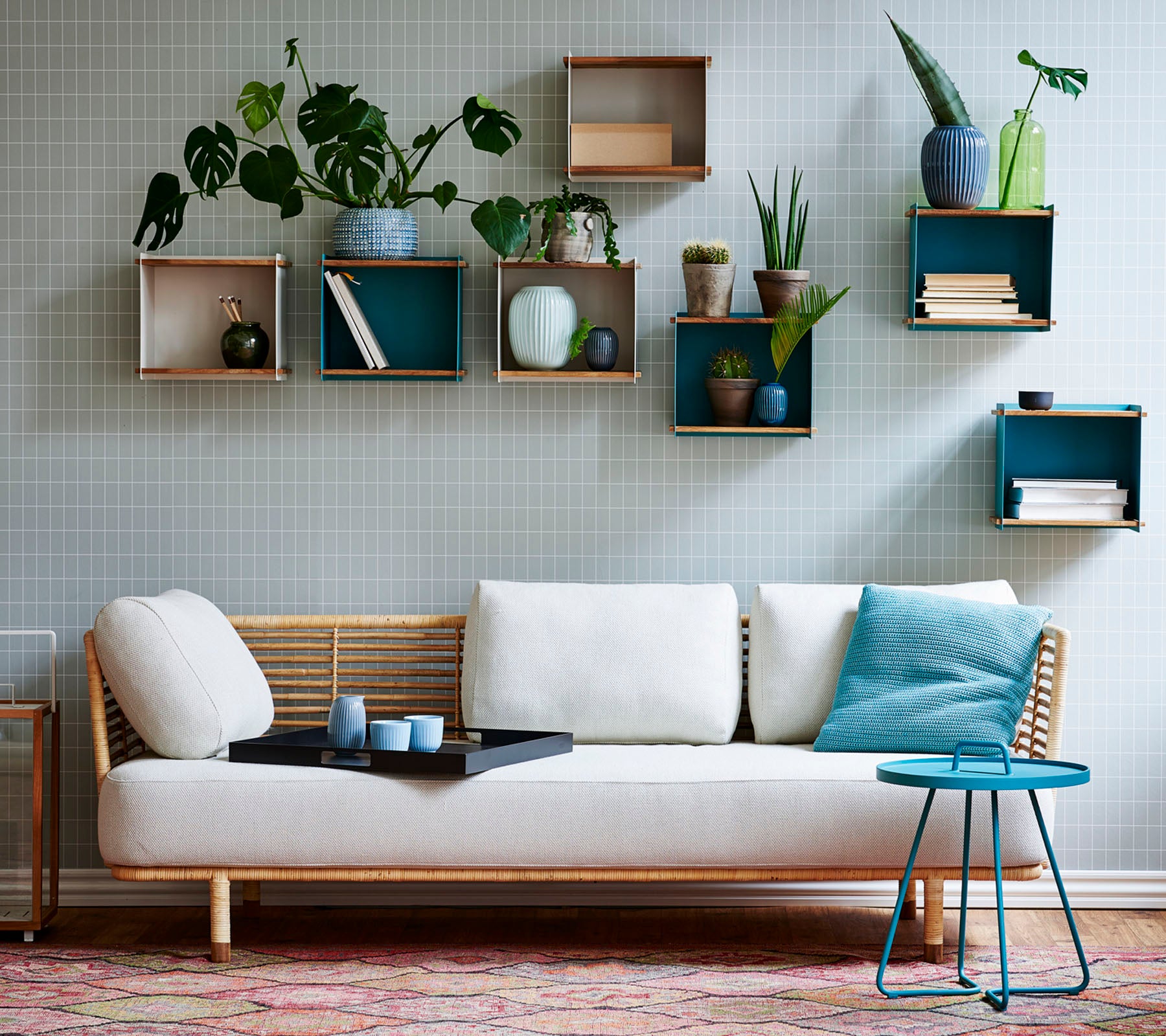 A stylish sofa with a light cushion and a small table, adorned with various potted plants displayed on geometric shelves.