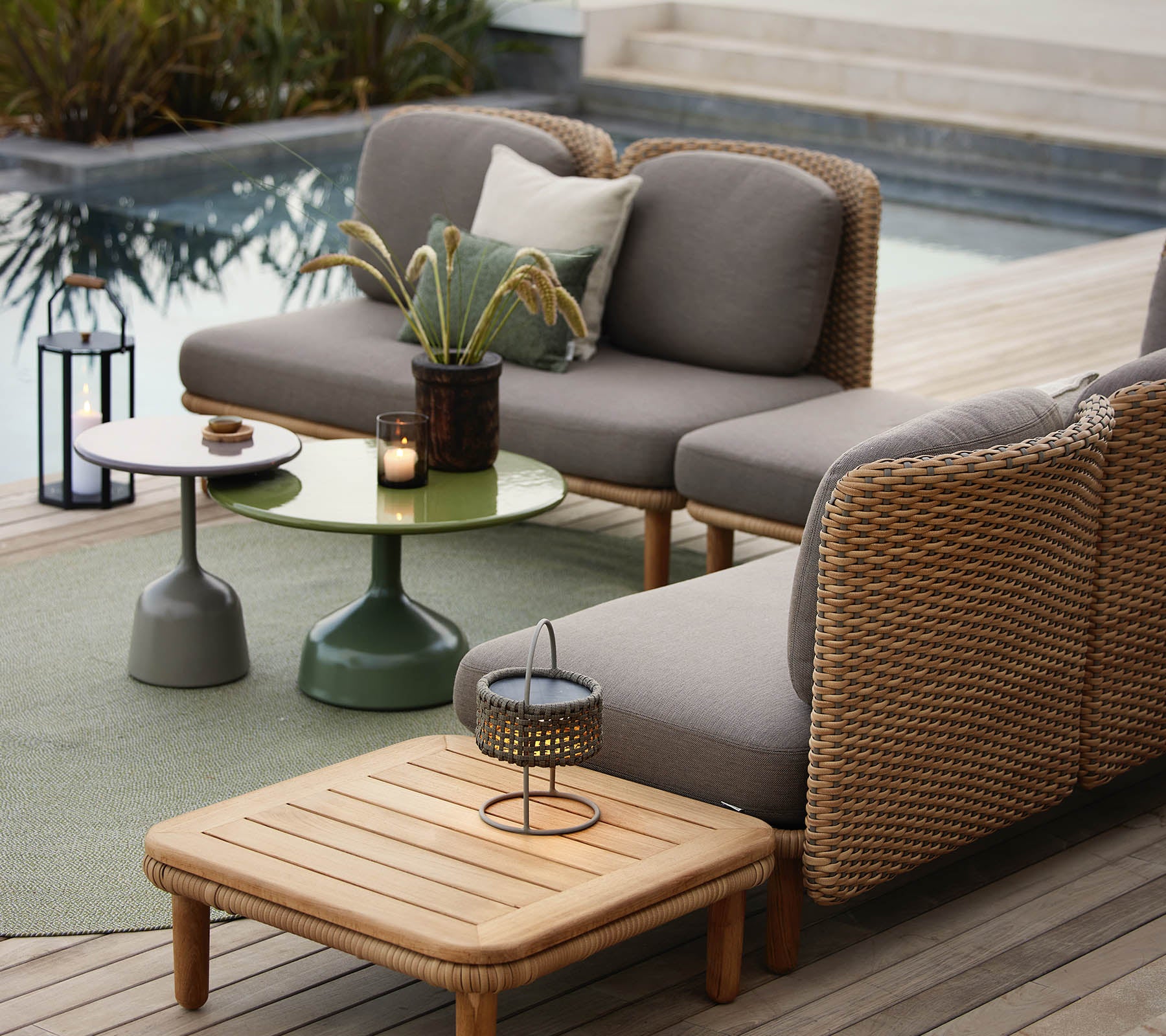 A stylish lounge seating area featuring a gray sofa with wicker accents, a green side table, and decorative accessories.