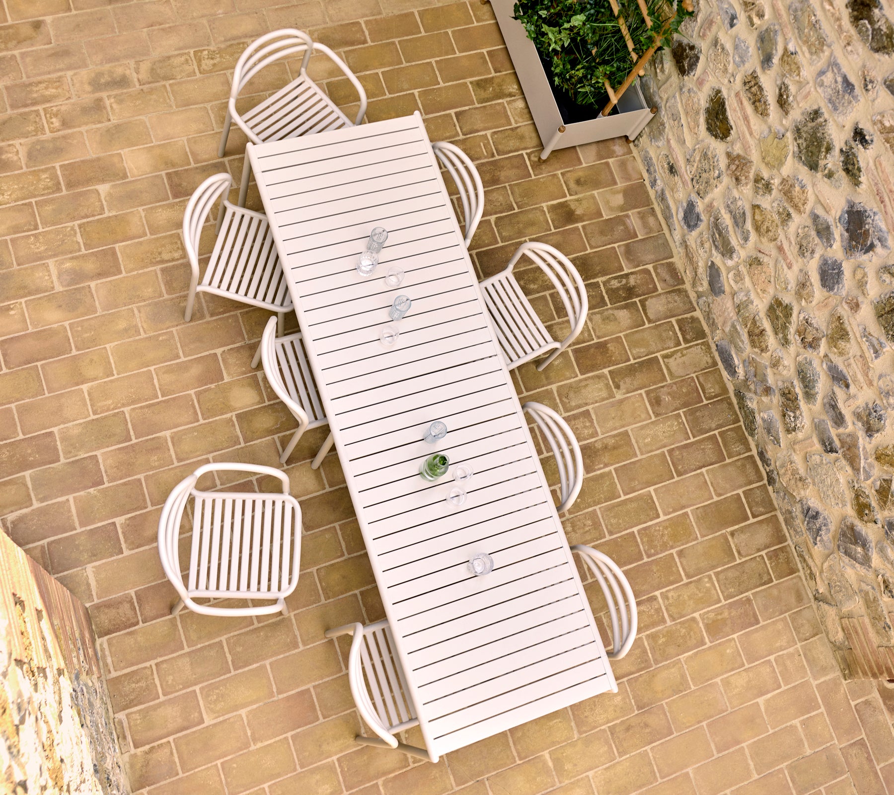 Aerial view of a sand-colored outdoor dining table with eight Bliss chairs, set on a stone-paved patio.