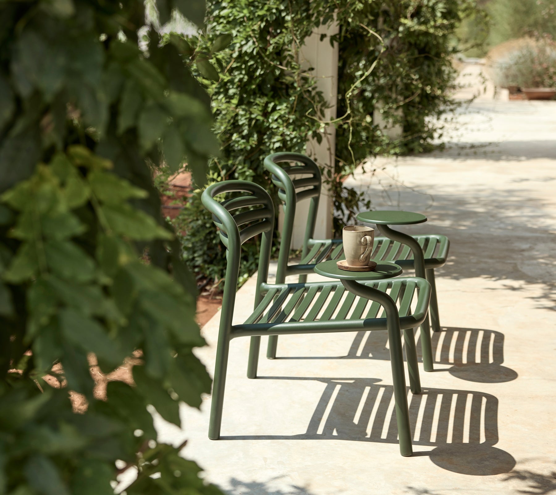 Green chairs and side table in an outdoor setting with lush greenery.
