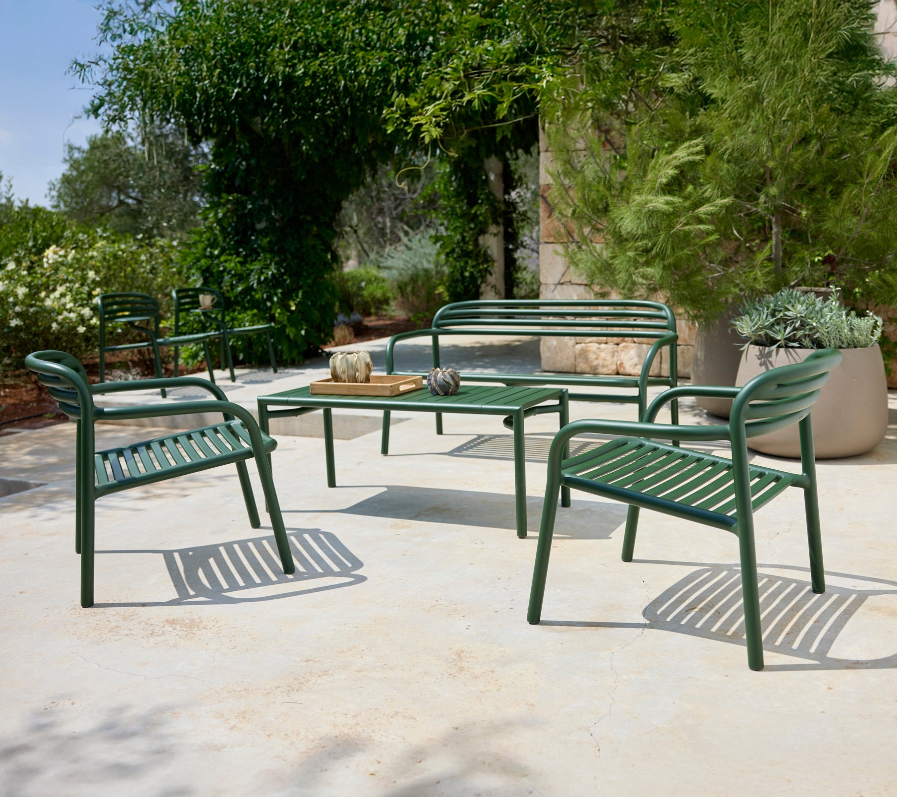 Green outdoor seating arrangement with chairs and bench surrounding a table.