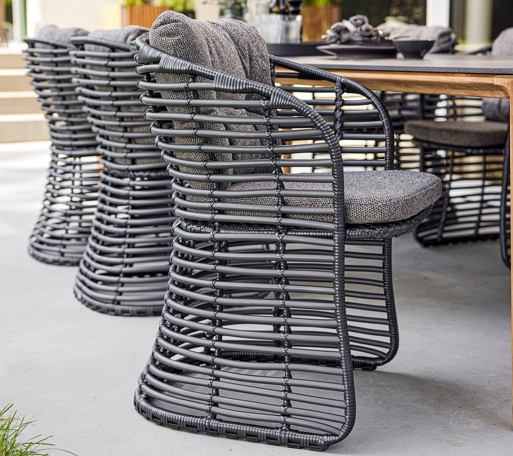 Stylish woven chairs with a modern design and cushioned seats, arranged beside a wooden table.