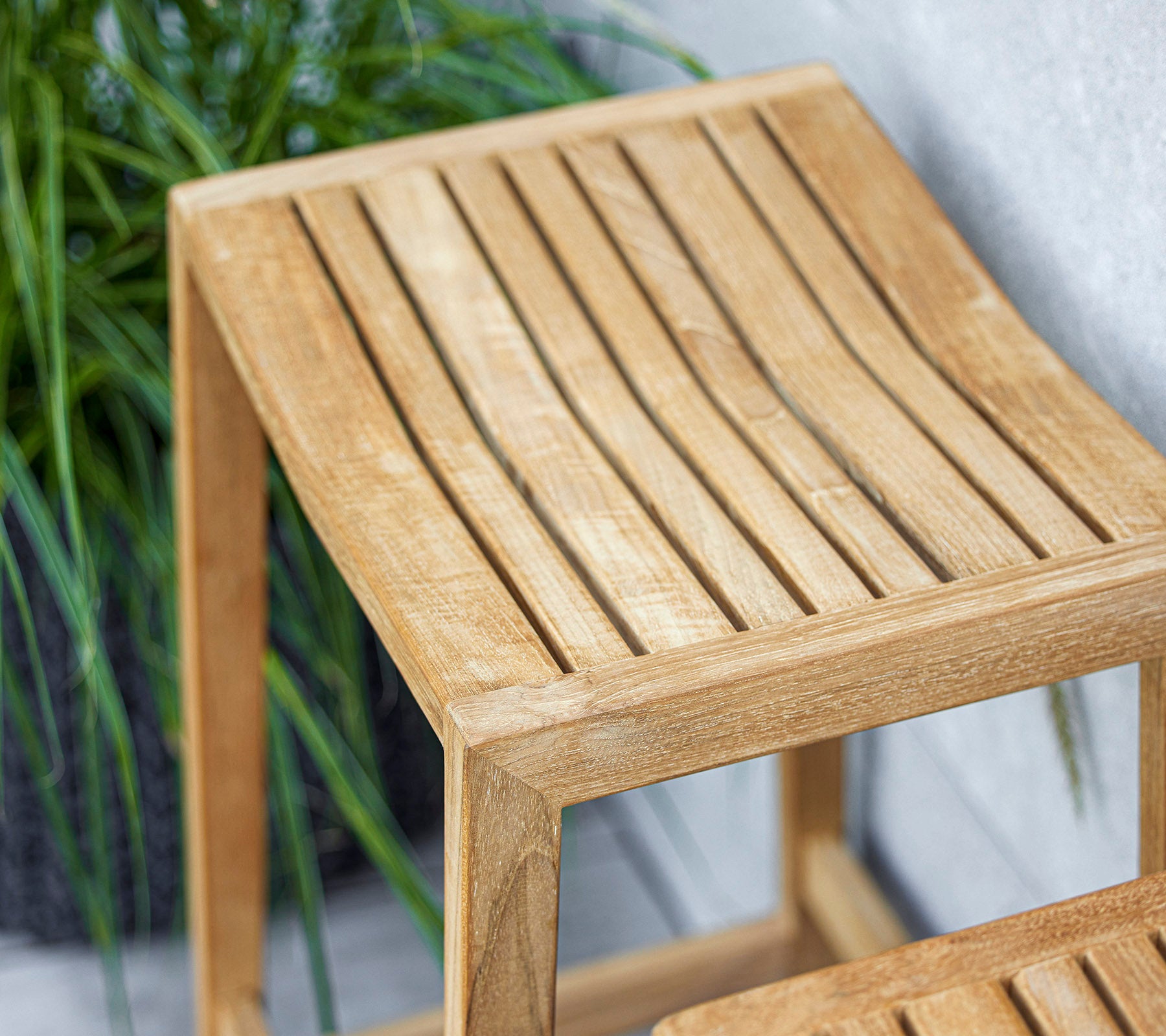 A sleek wooden side table with a slatted top design, featuring a light finish that complements surrounding greenery.