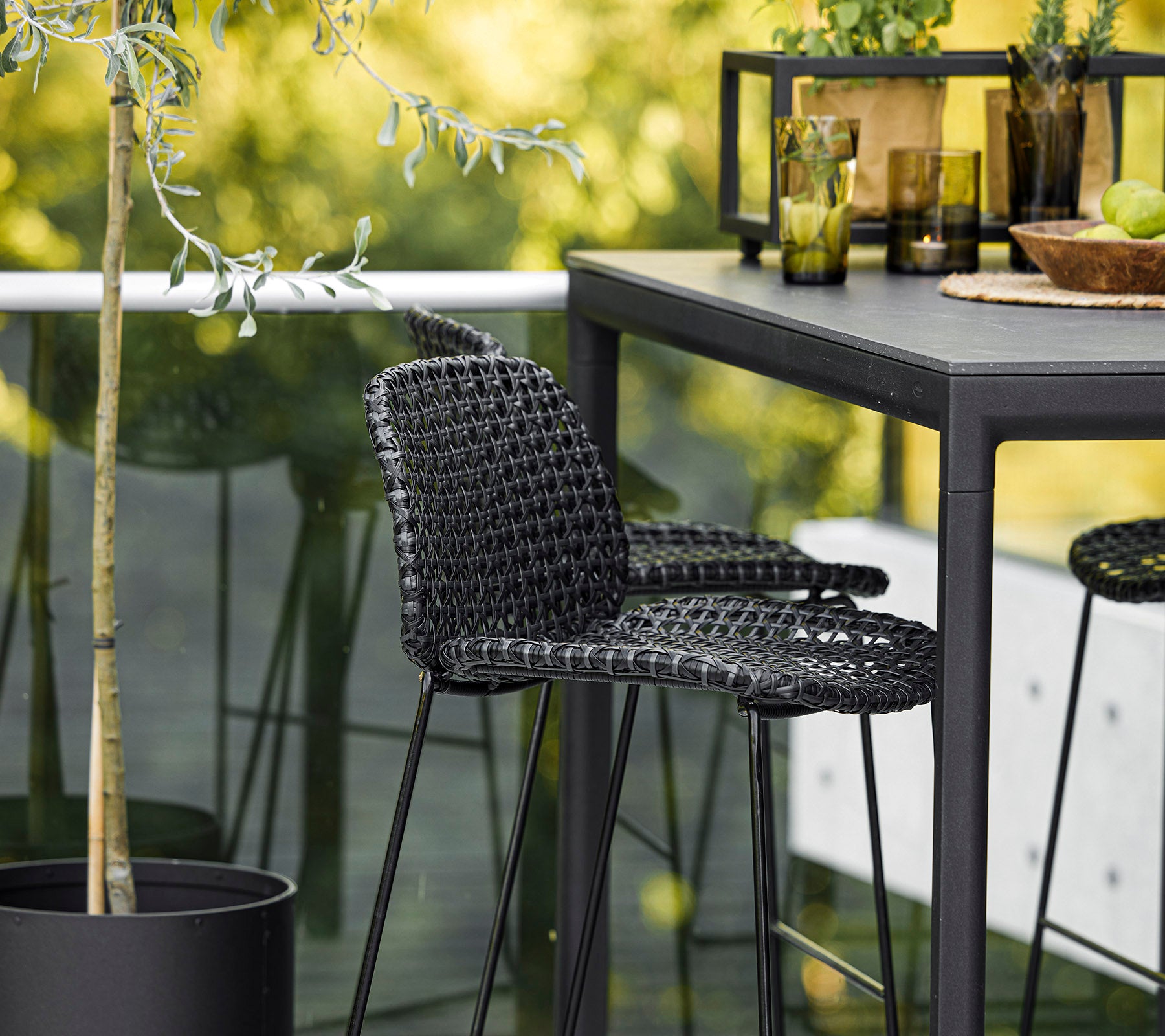 A stylish black woven chair paired with a sleek table, surrounded by decorative plants and glassware, creating a modern setting.