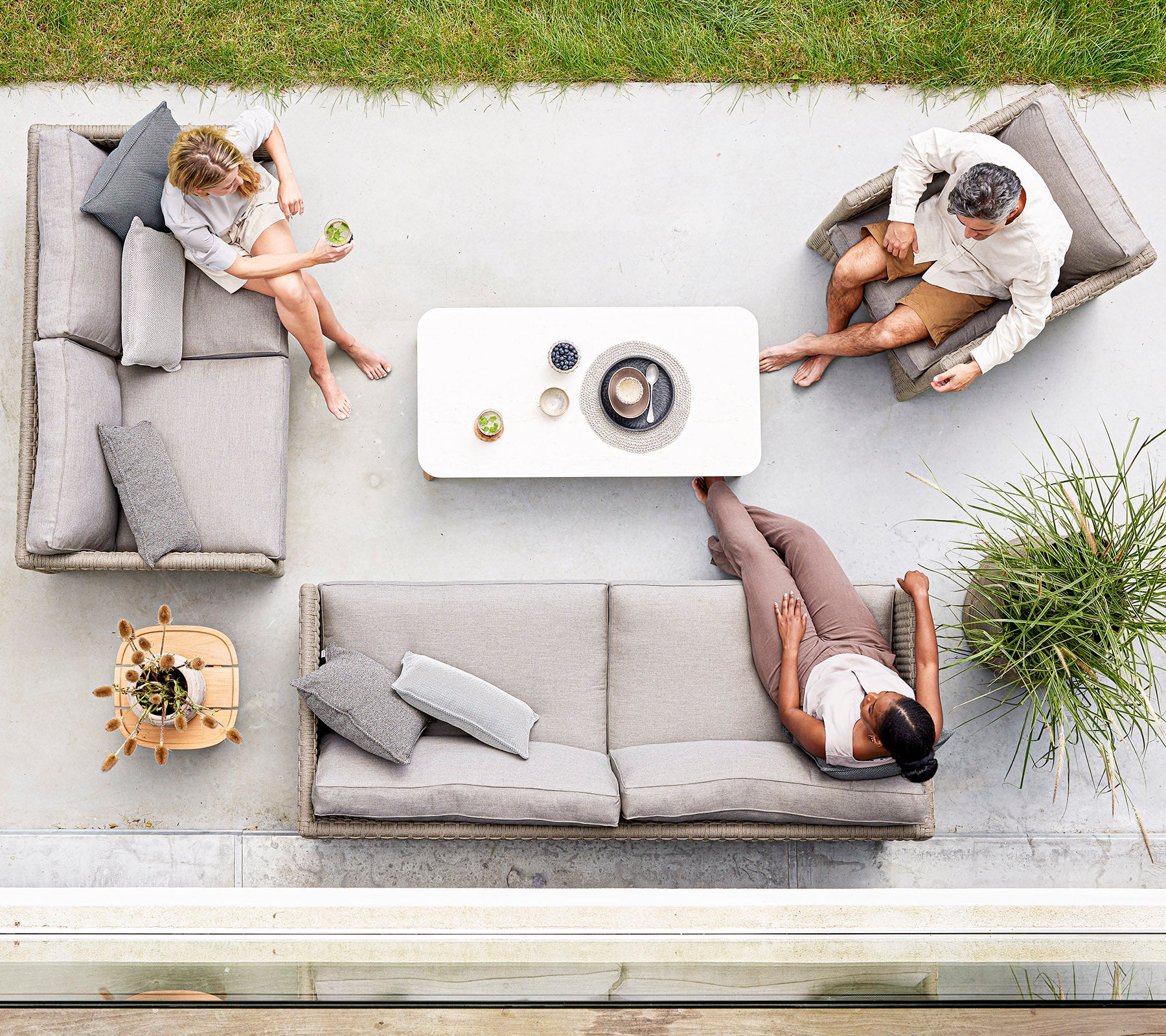 Three people relax on stylish light gray seating around a minimalist coffee table, enjoying drinks and conversation in a serene setting.