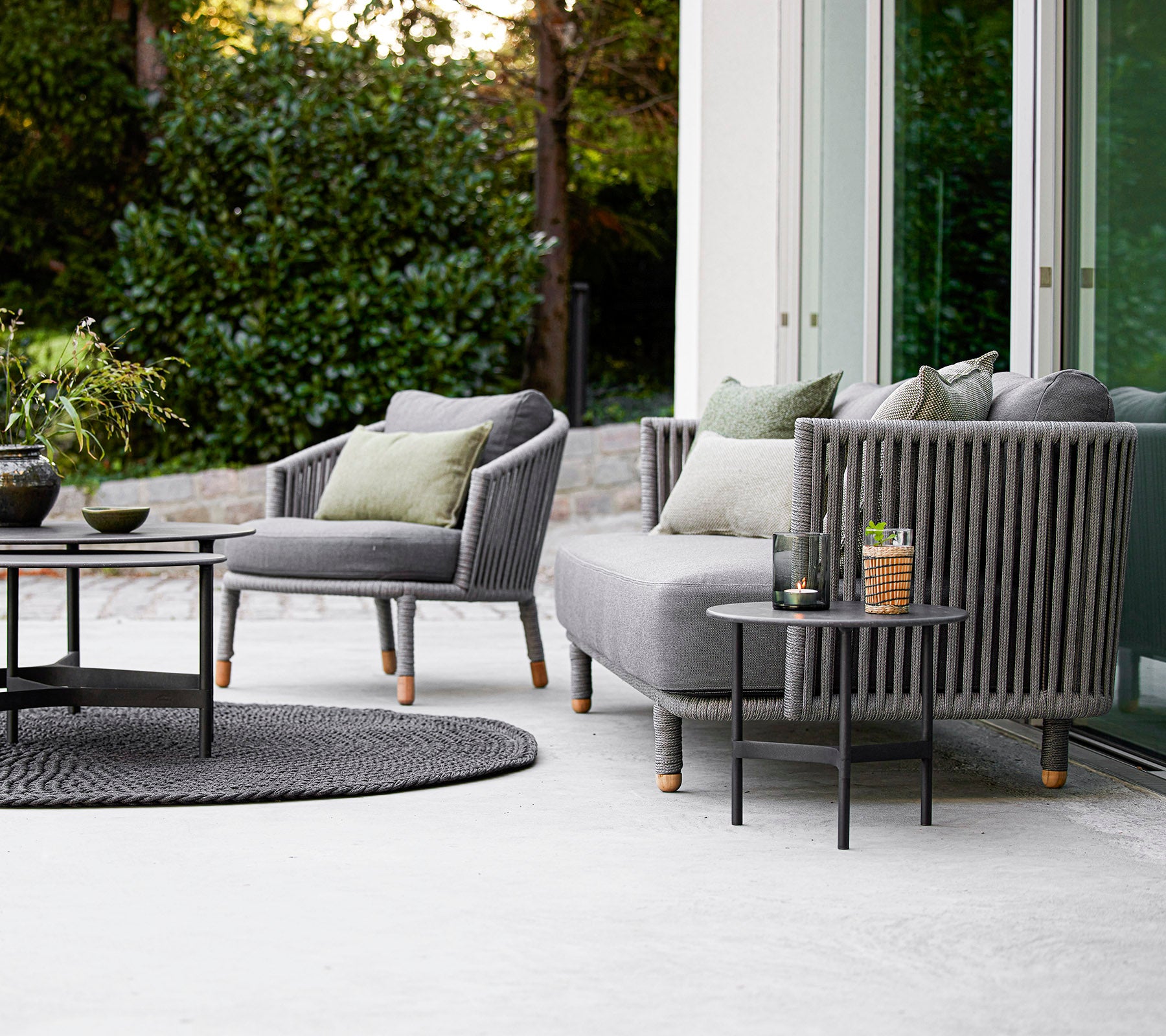 Contemporary outdoor seating set featuring a sofa and armchairs with cushions, paired with a round coffee table and decorative accessories.