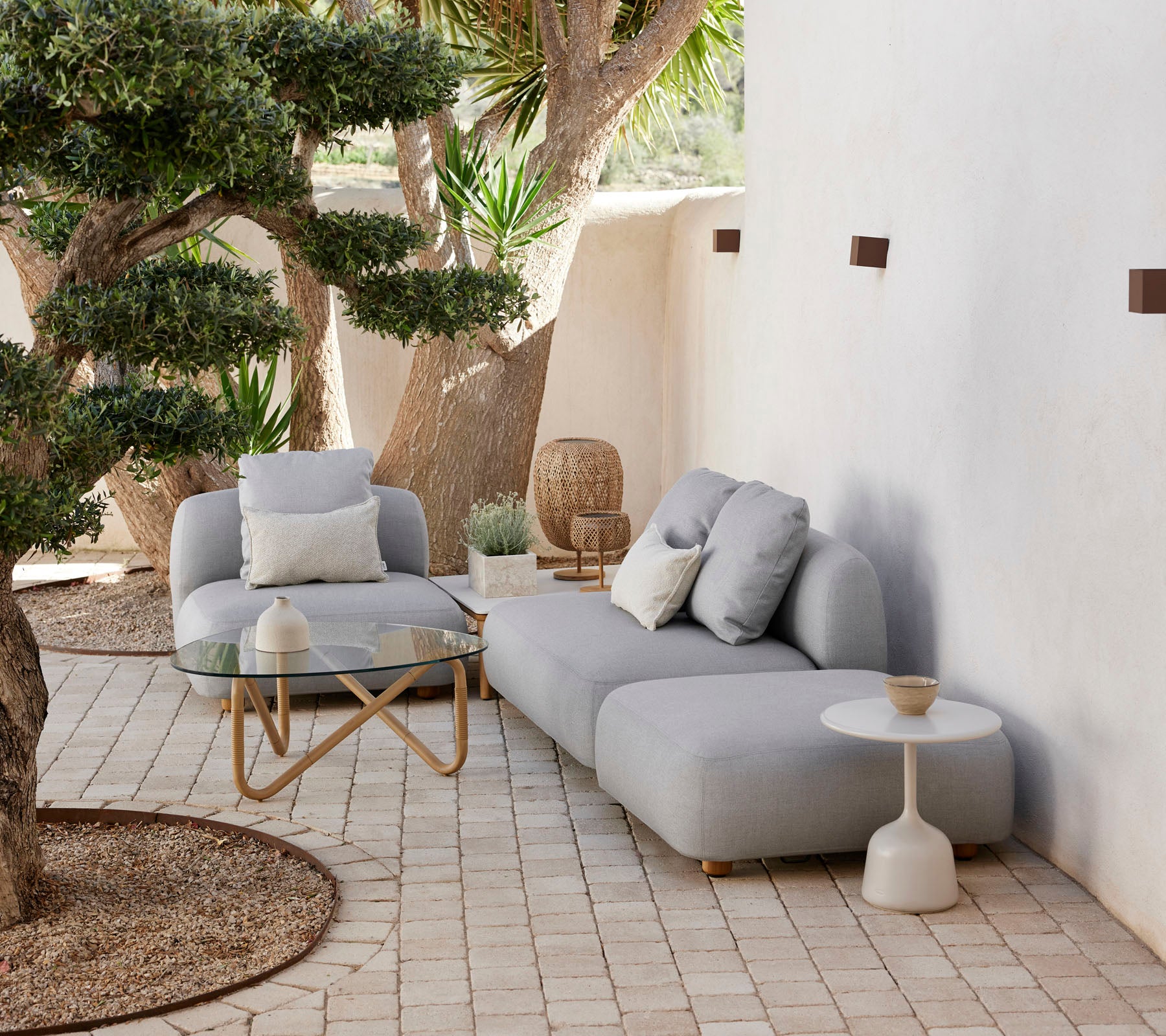 Modern outdoor seating arrangement with a cozy couch, accent chair, and stylish side table, surrounded by greenery and decorative elements.