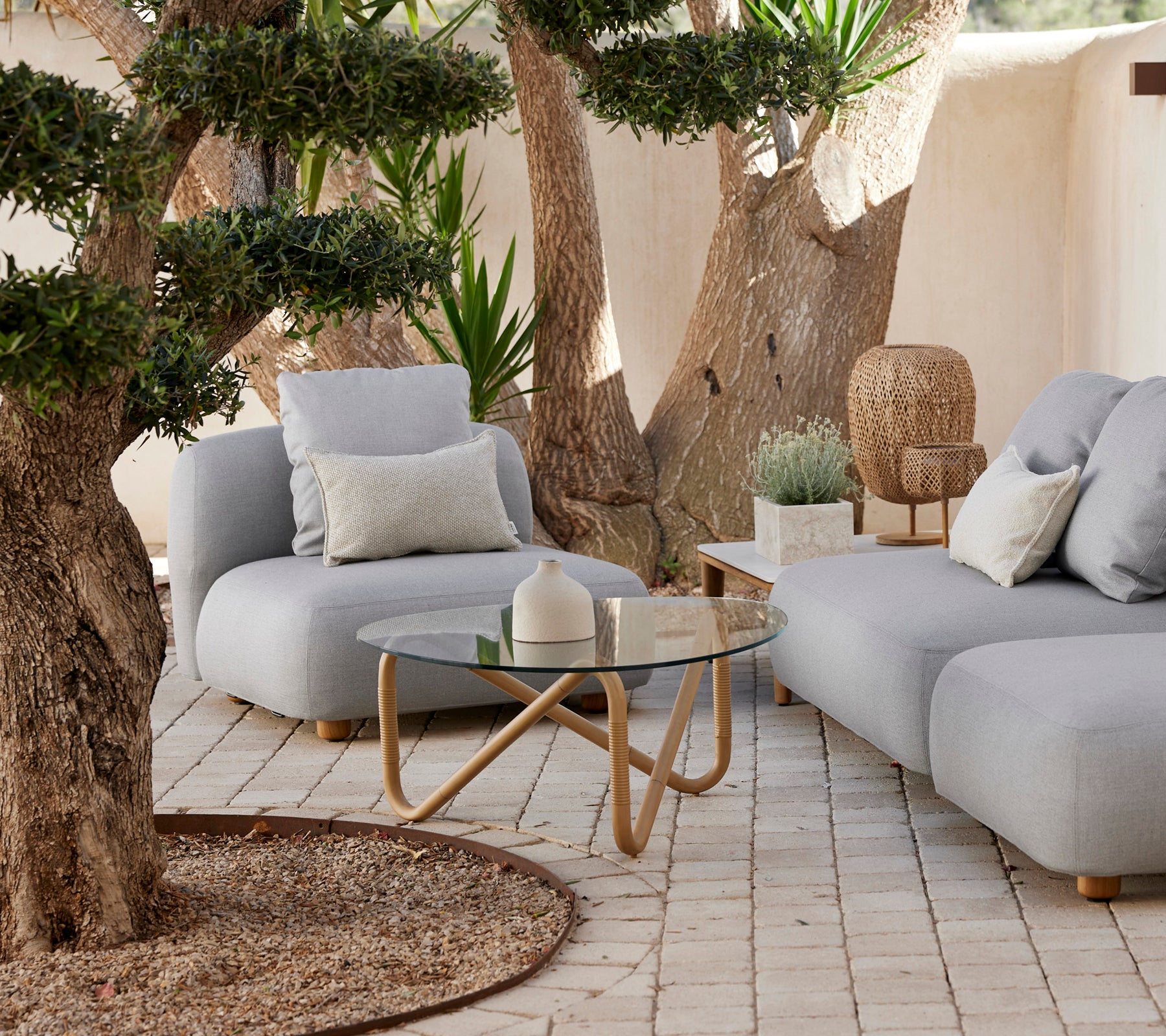 Modern grey sofa with cushions and a glass coffee table in a relaxed outdoor setting.