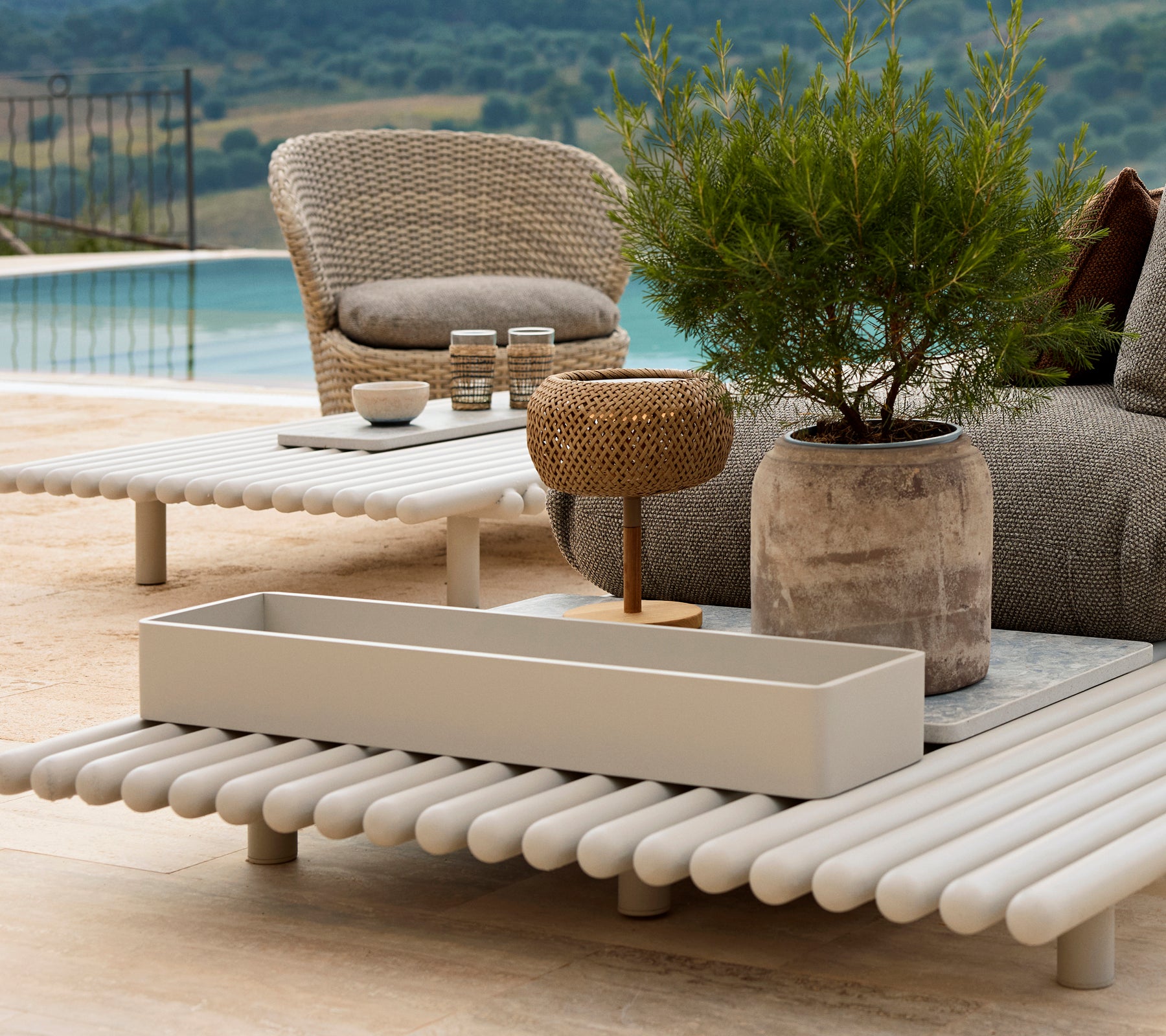 Aluminium storage box on a slatted table, surrounded by outdoor furniture and greenery, with a scenic view in the background.