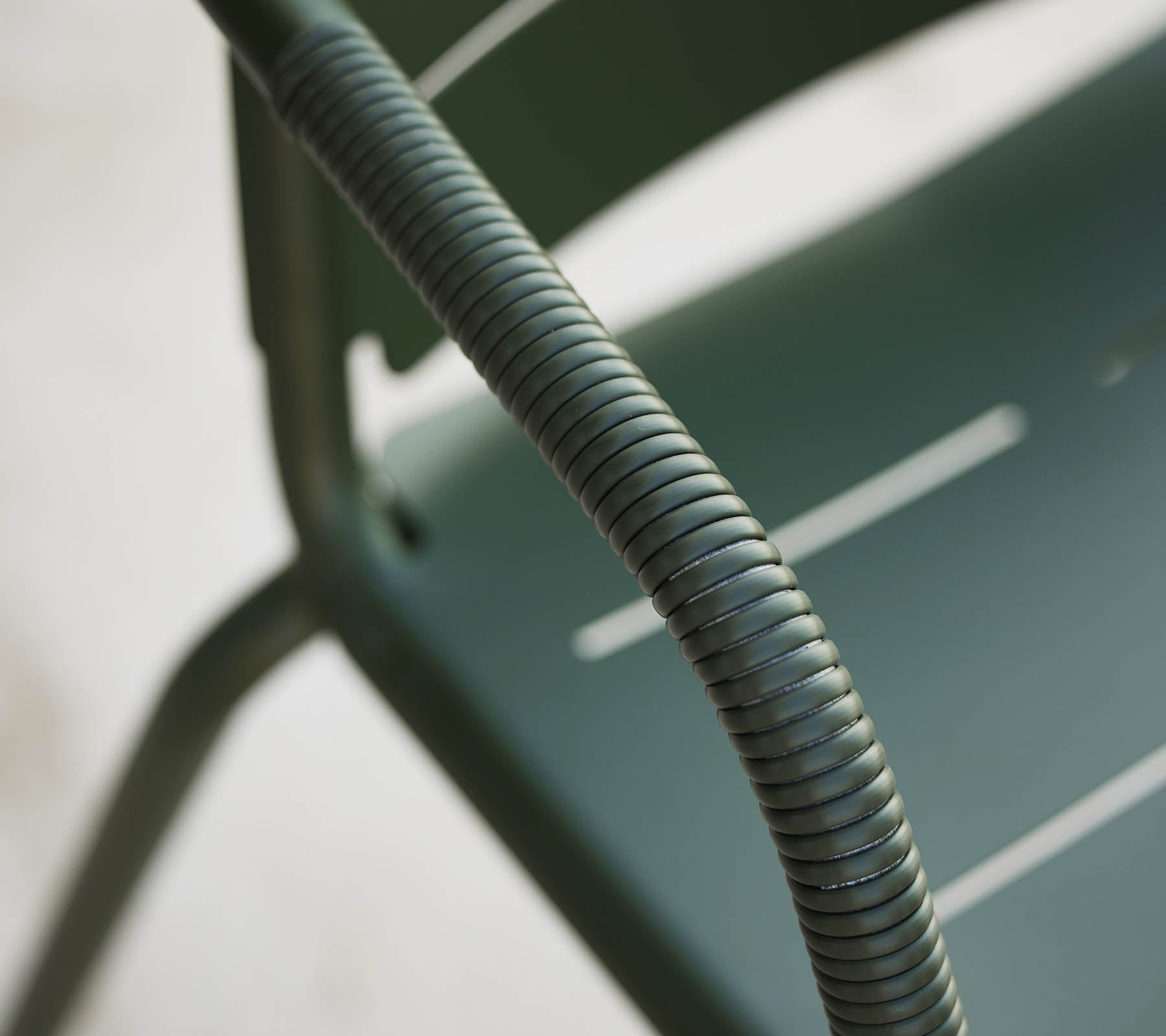Close-up of a green Copenhagen chair, highlighting its curved armrest and sleek design with subtle slats on the seat.