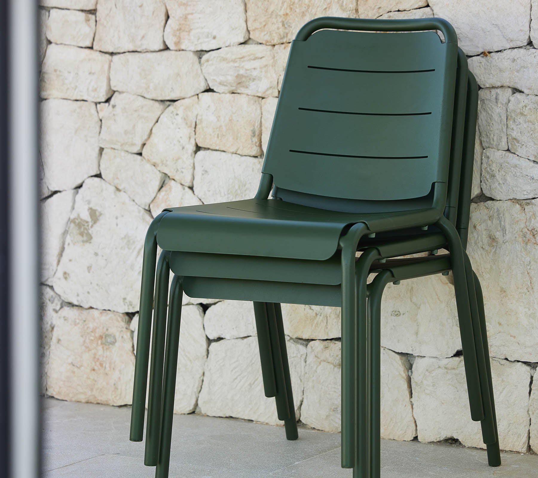 Stacked green Copenhagen chairs against a textured stone wall, showcasing a modern design and sleek, minimalist aesthetic.