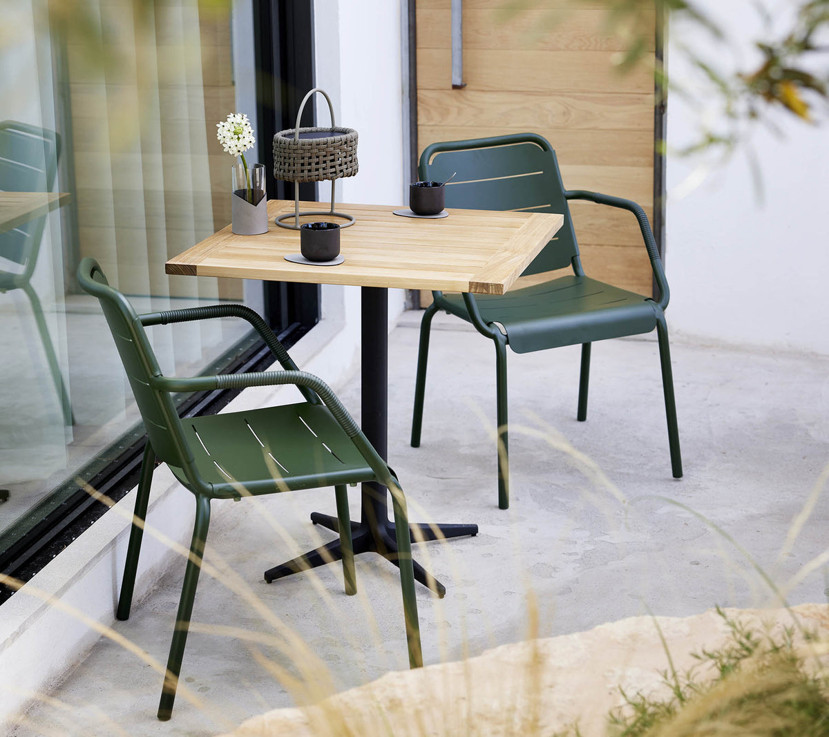 A minimalistic setting with a wooden table and green chairs, featuring a small flower arrangement and decorative lantern.