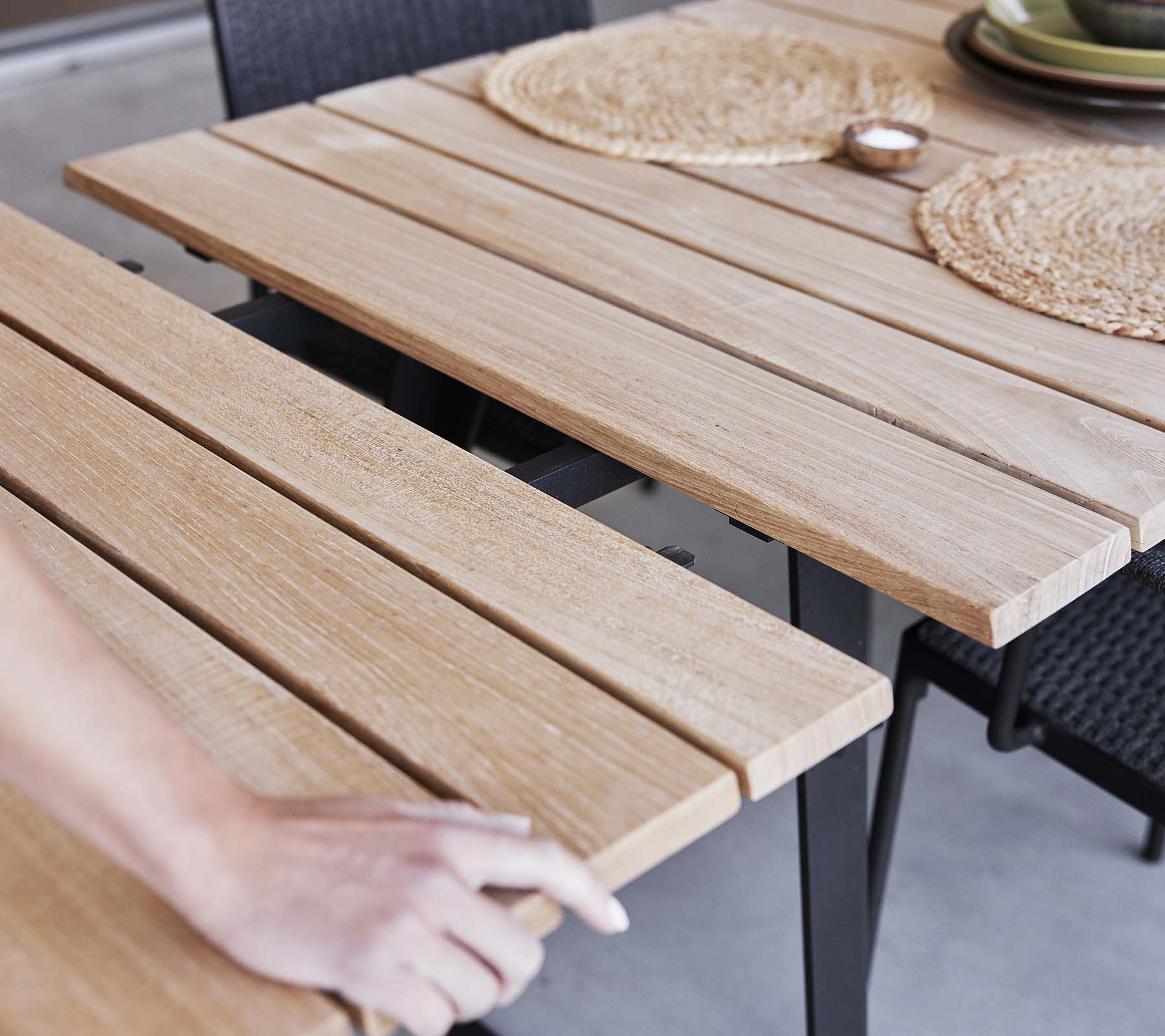 Detail of a wooden table featuring slatted design, placemats, and a minimalist aesthetic, perfect for dining or gatherings.