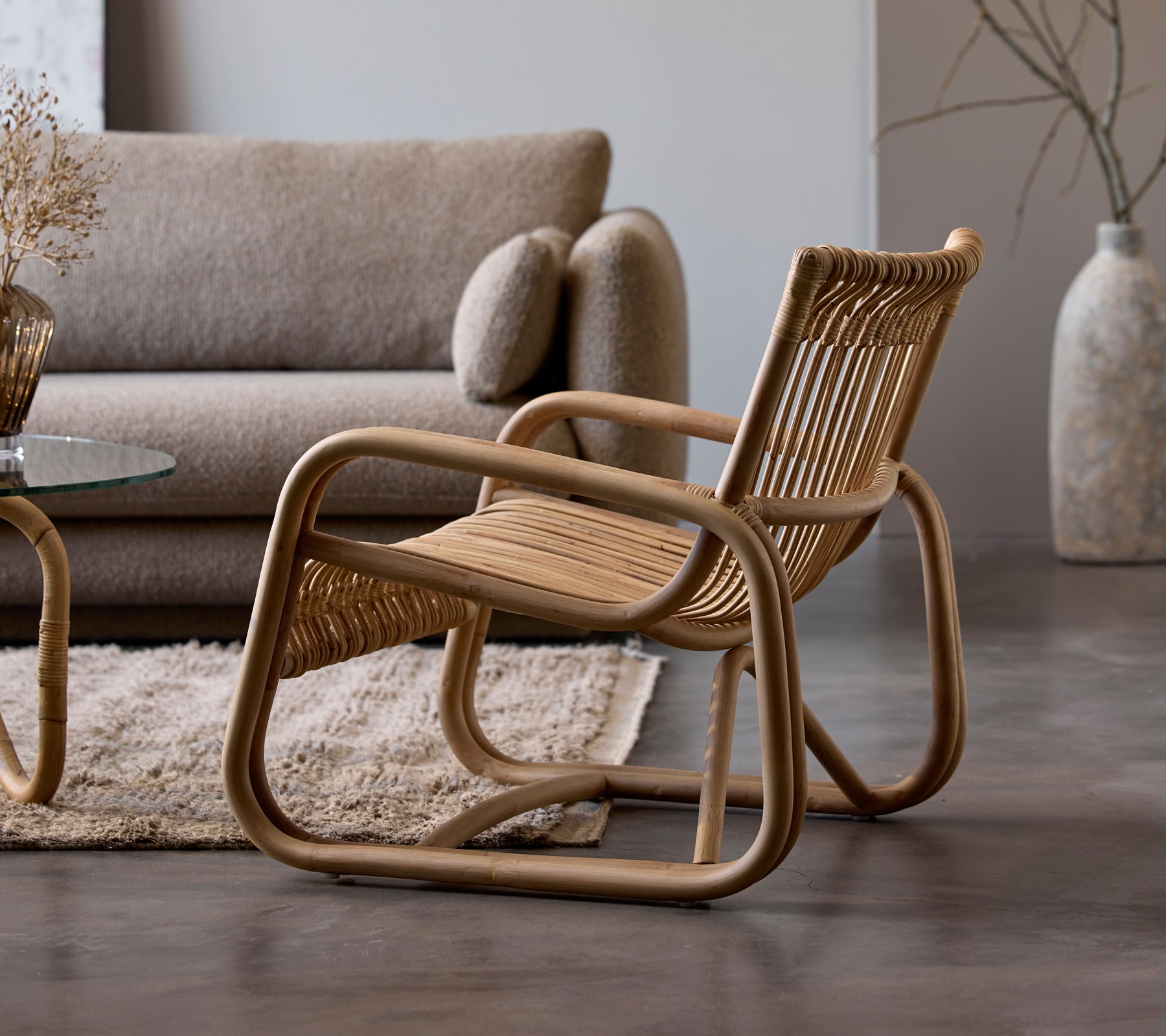 Rattan chair beside a beige sofa and glass table in a modern lounge setting.