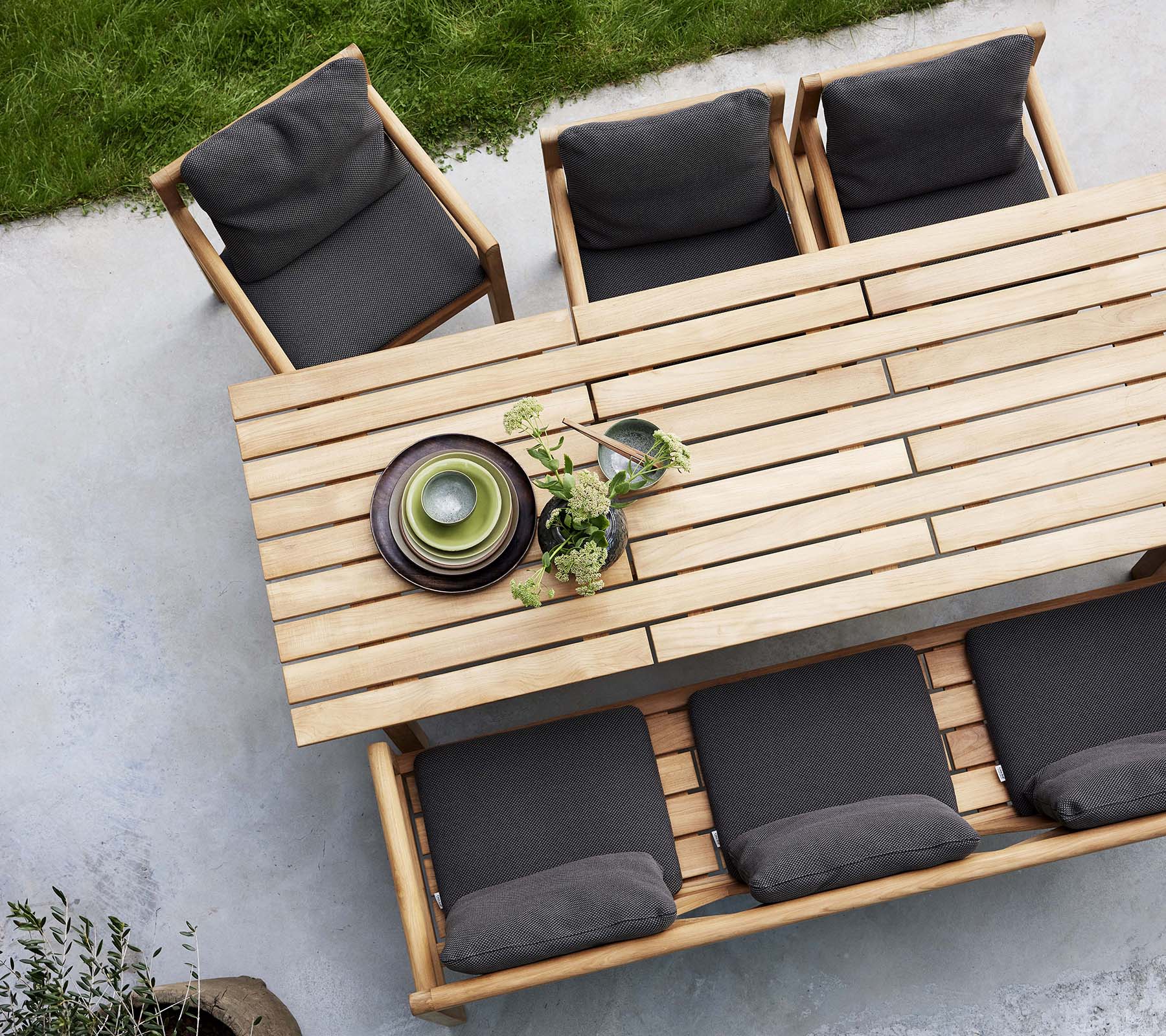 A wooden dining set featuring a table, bench, and chairs with dark cushions, accented by decorative plates and greenery.