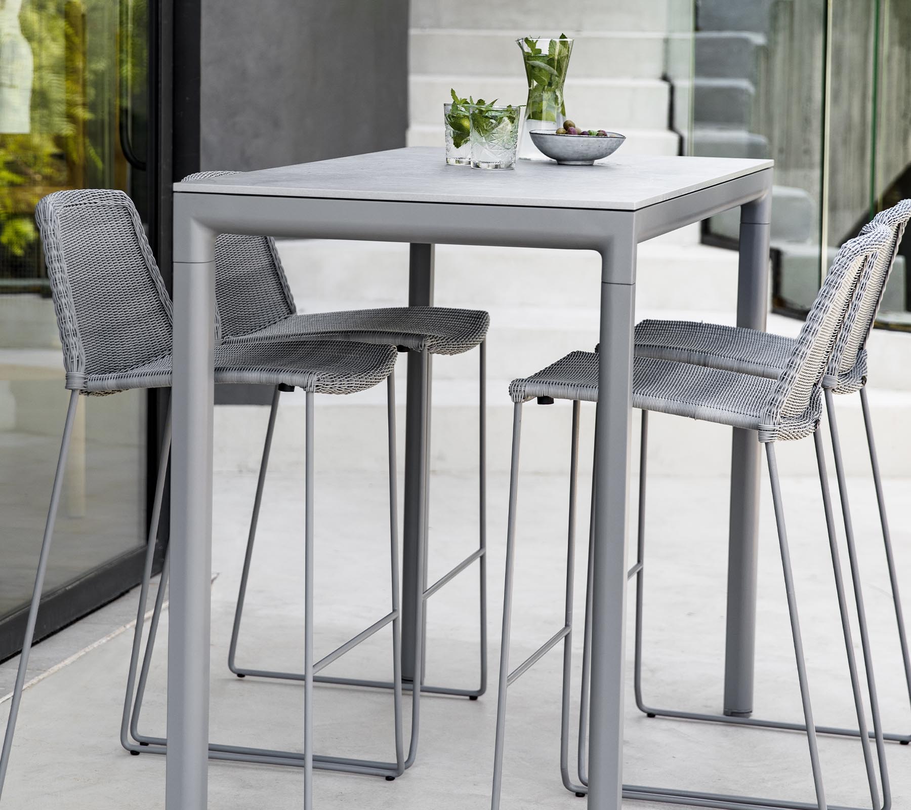 A modern gray table with three matching stools, featuring decorative plants and a bowl on the table's surface.