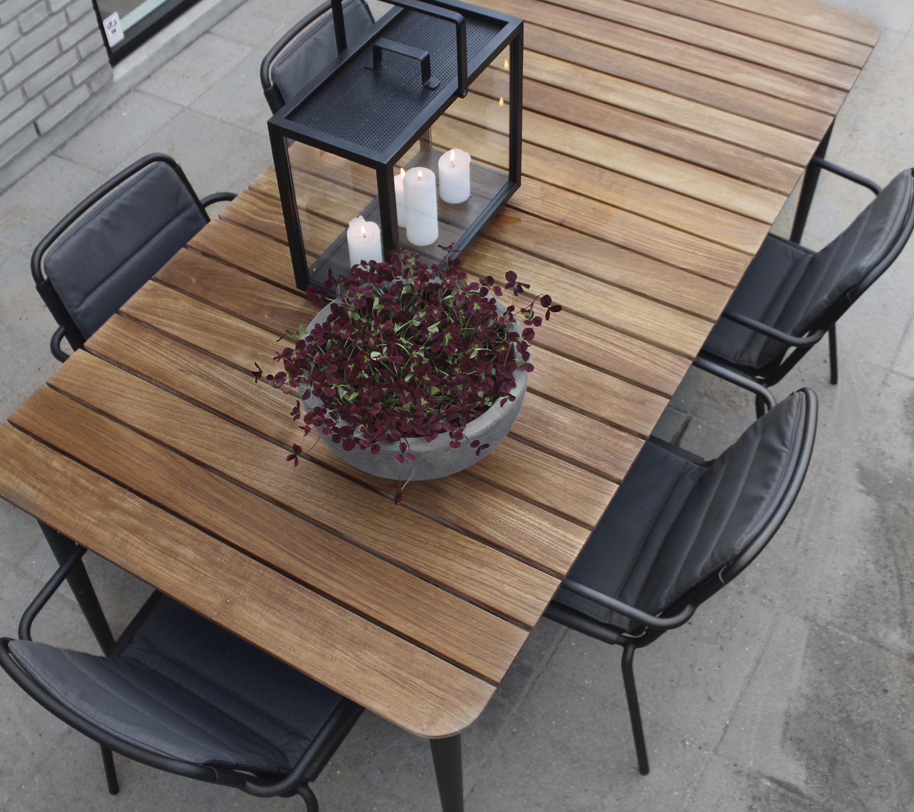 A wooden table with black chairs, featuring a large planter and a candle lantern centerpiece.