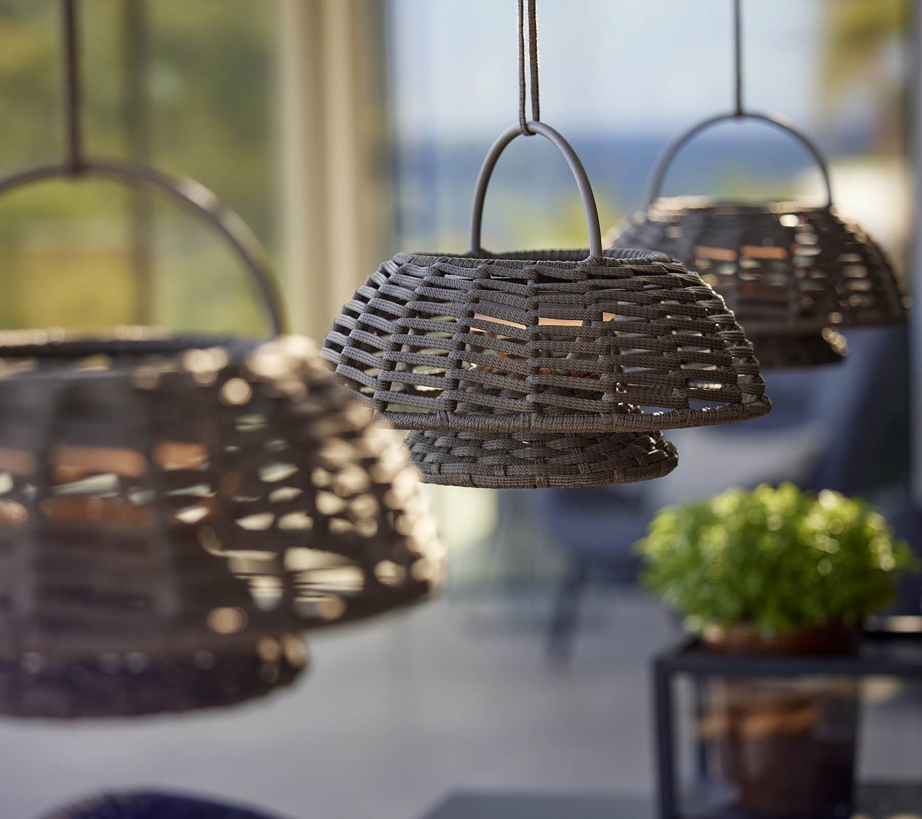 Three woven lamps hanging in a row, creating a warm and inviting atmosphere, complemented by a small potted plant.
