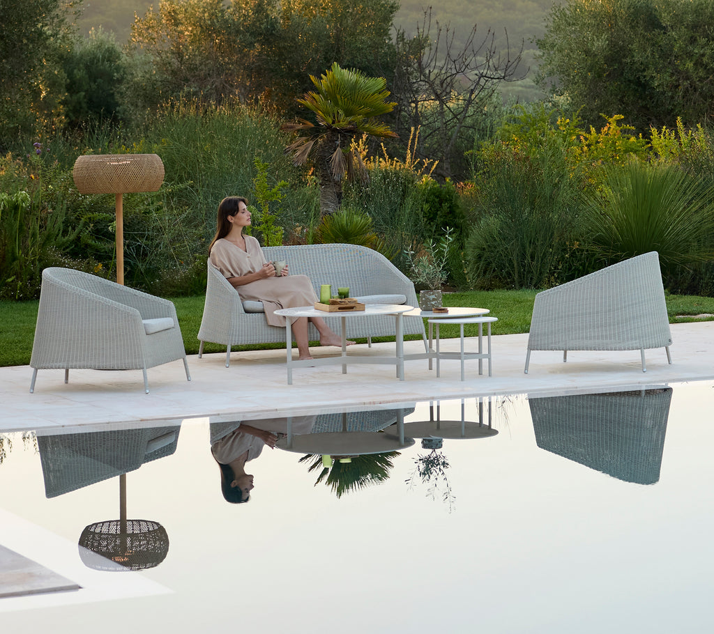Modern grey sofa and armchairs surrounding a white table in a relaxing outdoor lounge.
