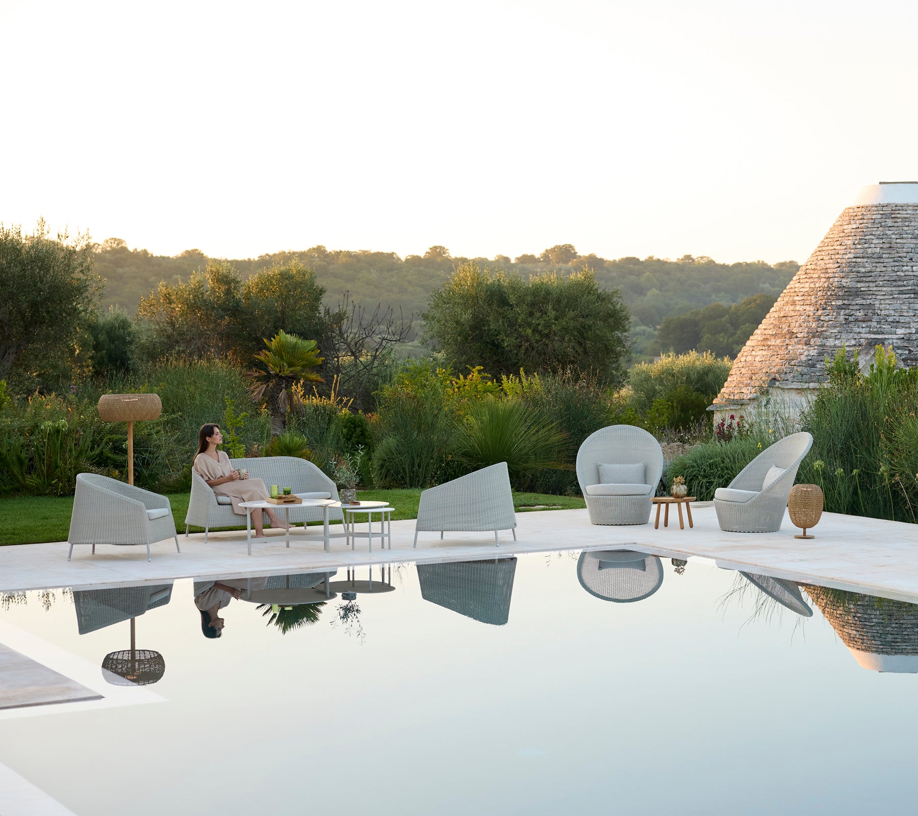 Modern outdoor lounge area with grey chairs and a white table by a pool.