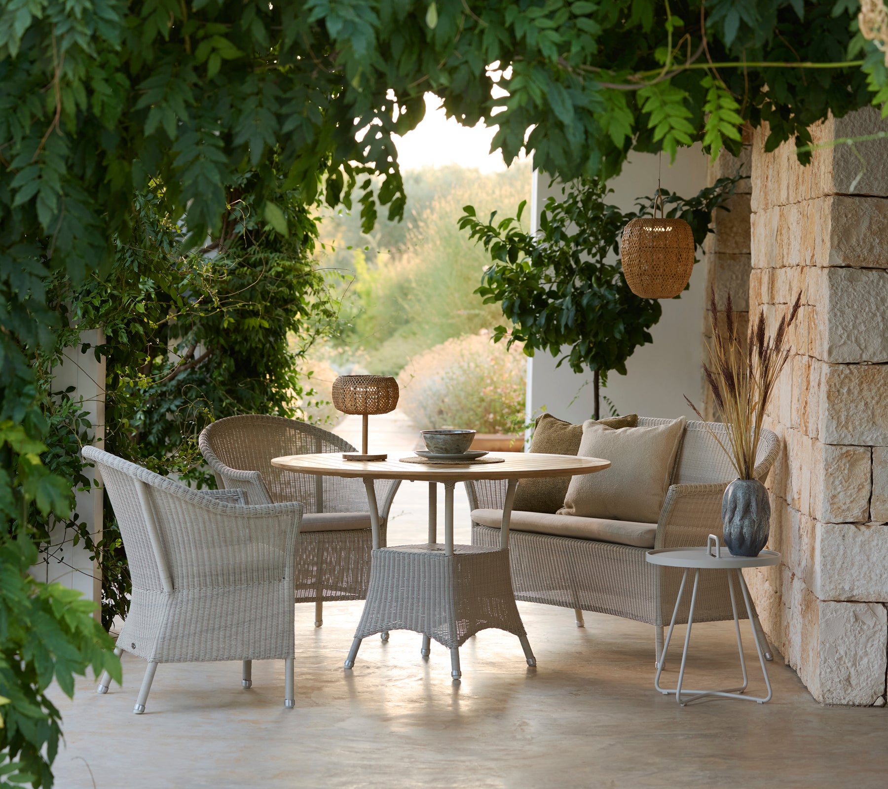 Contemporary lounge furniture set featuring woven chairs, round table, and cushions in a serene outdoor setting.