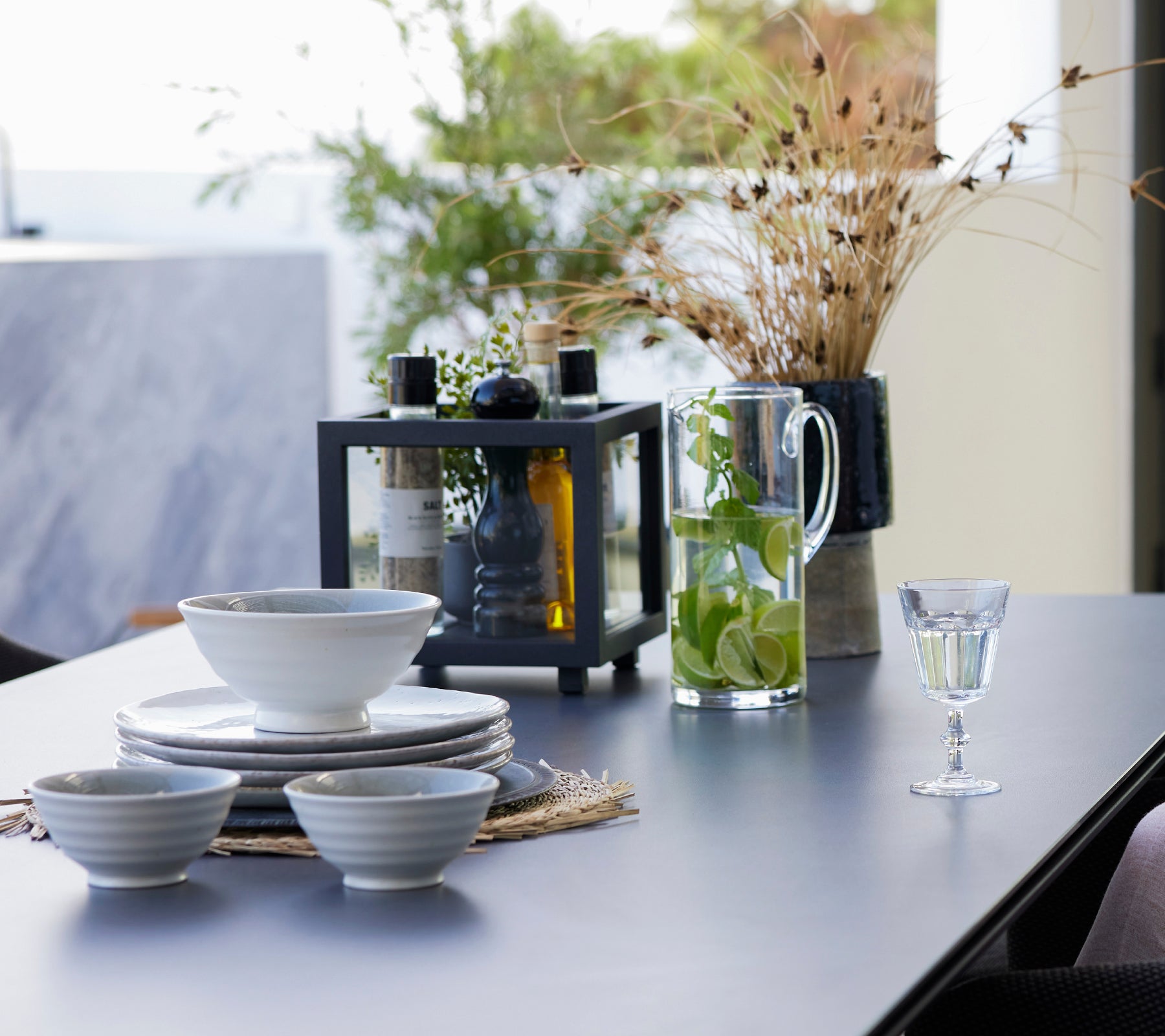 Dining table set with white bowls, black lantern, glass pitcher, and drinks.