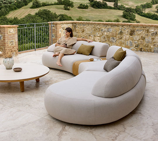 A mellow curved sofa with cushions and a wooden coffee table, accompanied by a person sitting comfortably while enjoying the view.